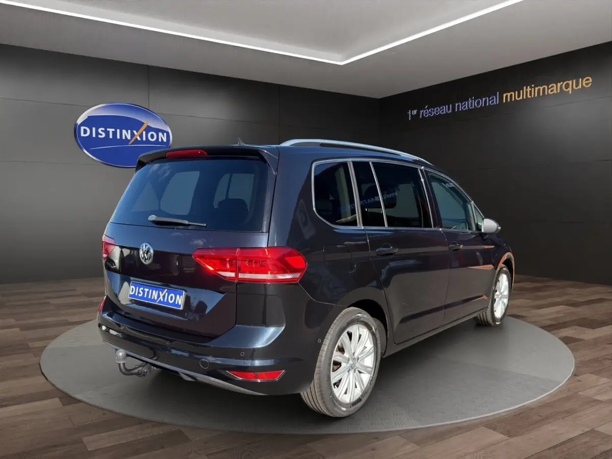 Volkswagen Touran noir vue 3/4 arrière droit avec attelage, en intérieur sur plateforme rotative.