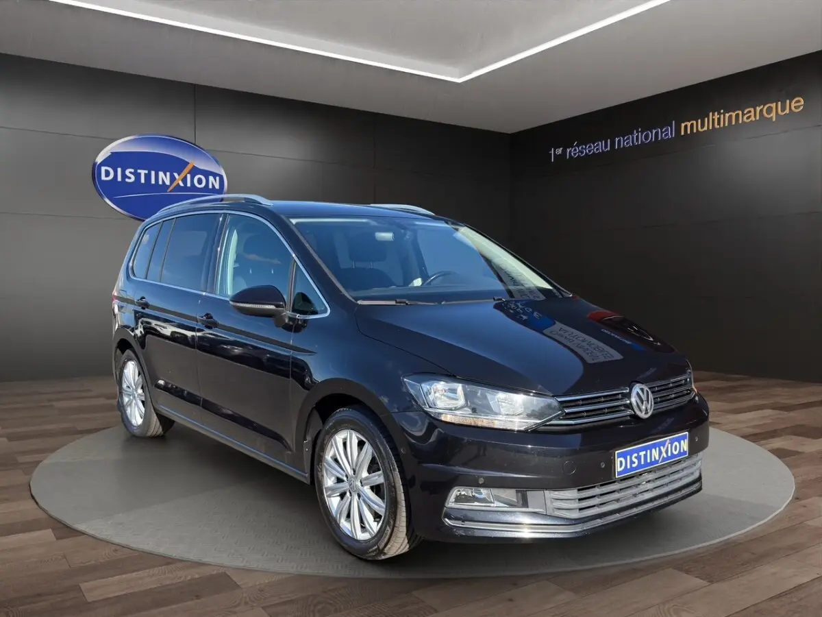 Volkswagen Touran noir en 3/4 avant droit, avec jantes alliage et calandre chromée visible en showroom.