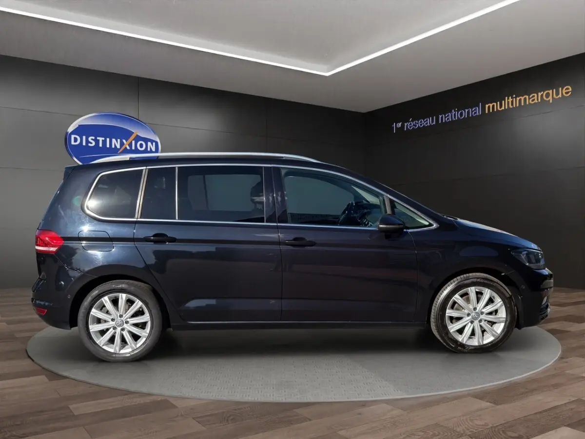 Profil droit d’un Volkswagen Touran noir 2016 avec jantes alliage et barres de toit chromées en showroom.