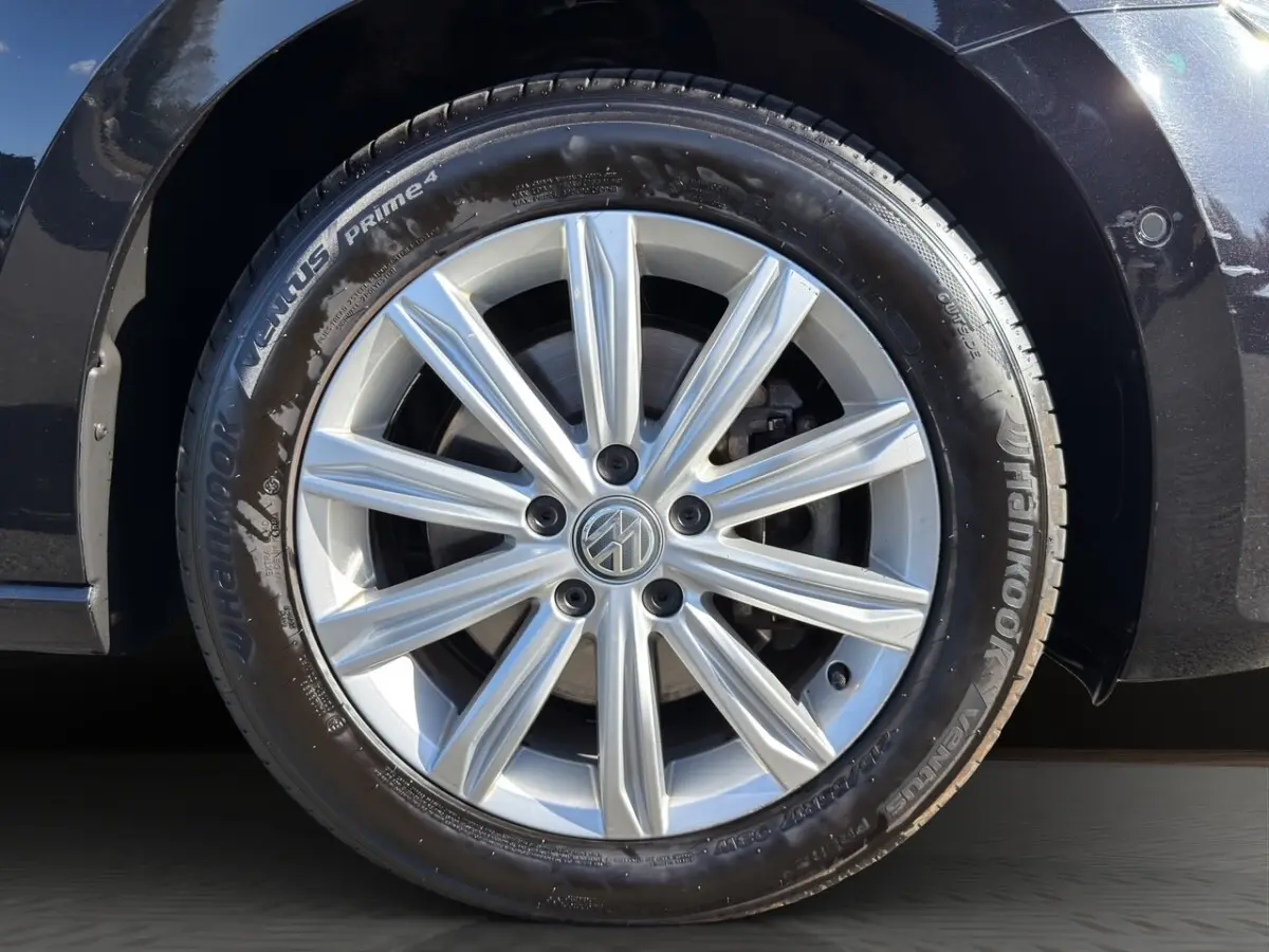 Gros plan sur la roue avant droite d’un Volkswagen Touran noir, avec jante alliage argentée à dix branches.