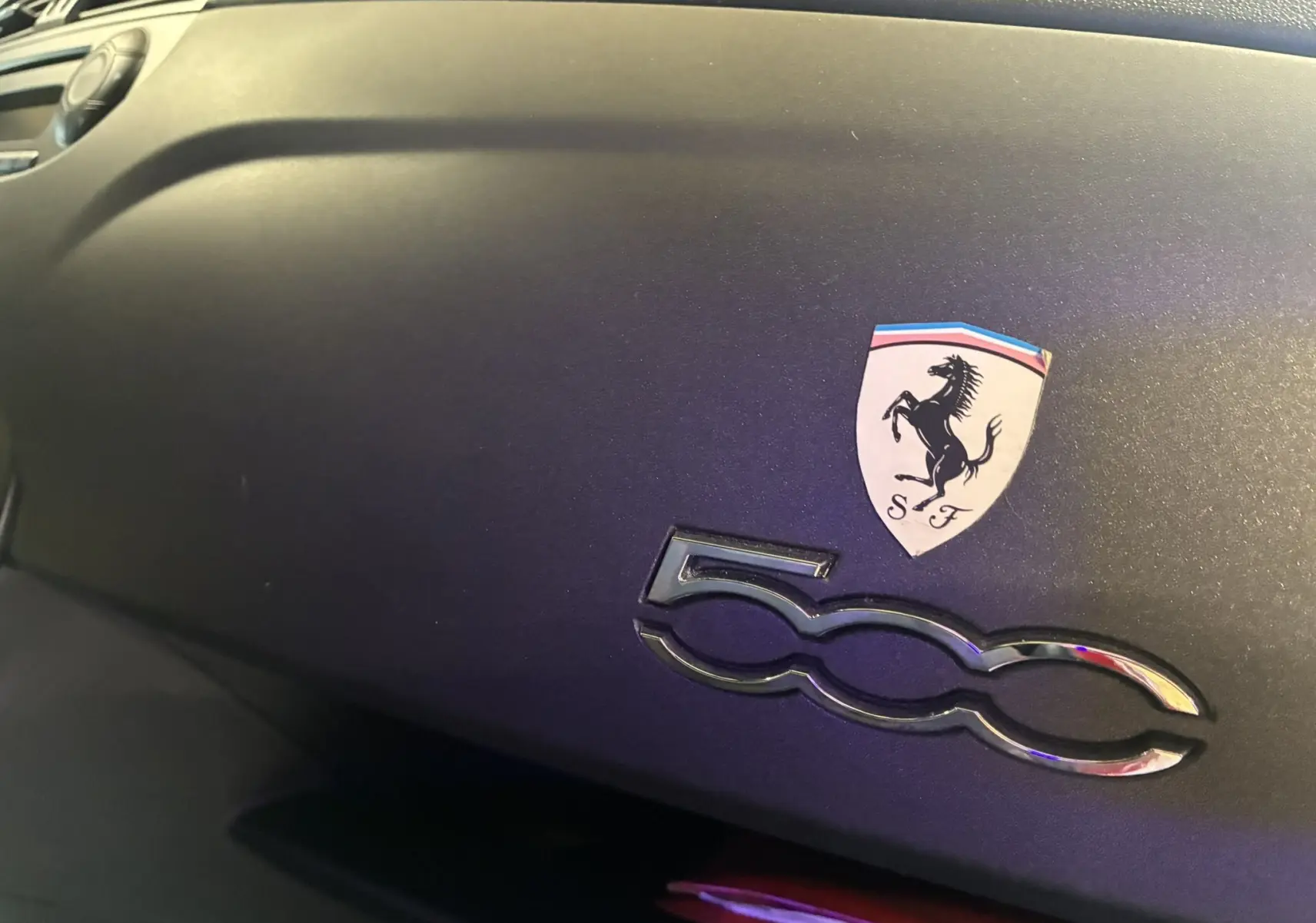 Détail intérieur du tableau de bord noir de l'Abarth 500 avec logo 500 chromé et écusson Ferrari.
