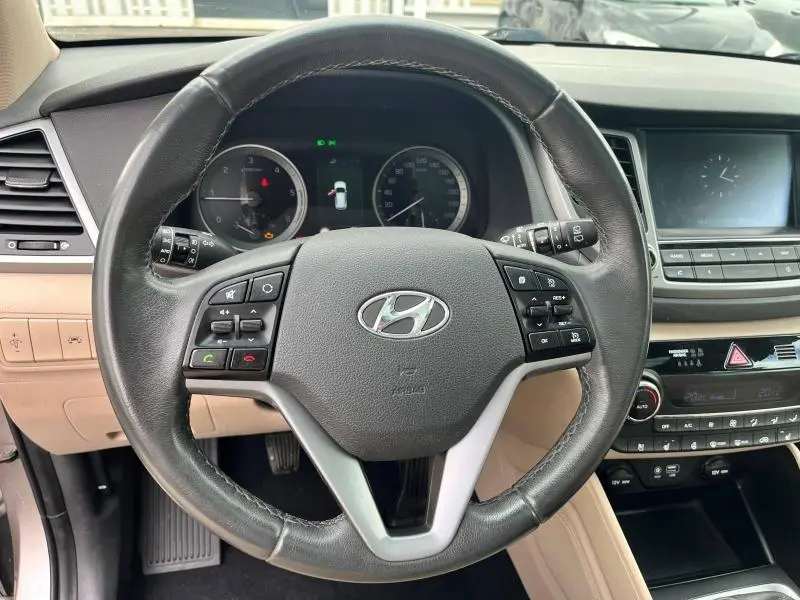 Volant cuir noir vu de face dans l'habitacle beige du Hyundai Tucson 2017 avec commandes multifonctions intégrées.