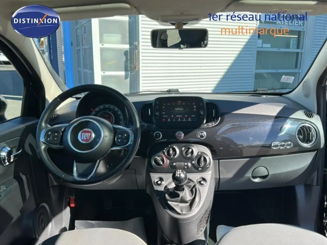 Vue intérieure frontale du tableau de bord noir brillant de la Fiat 500 Lounge 2016 avec volant multifonction et levier de vitesse manuel.