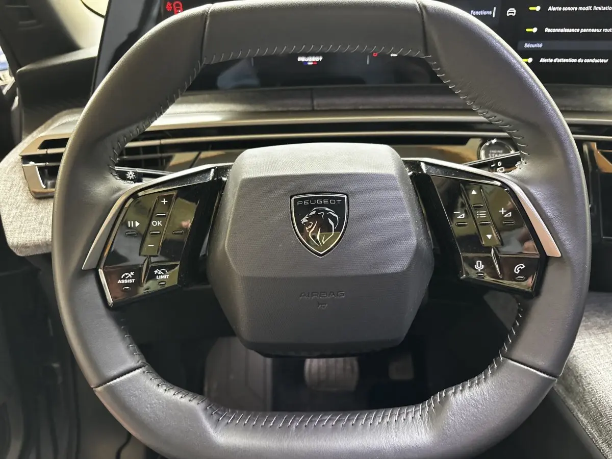 Gros plan sur le volant cuir noir du Peugeot 5008 2025 avec commandes multifonctions et logo lion central.
