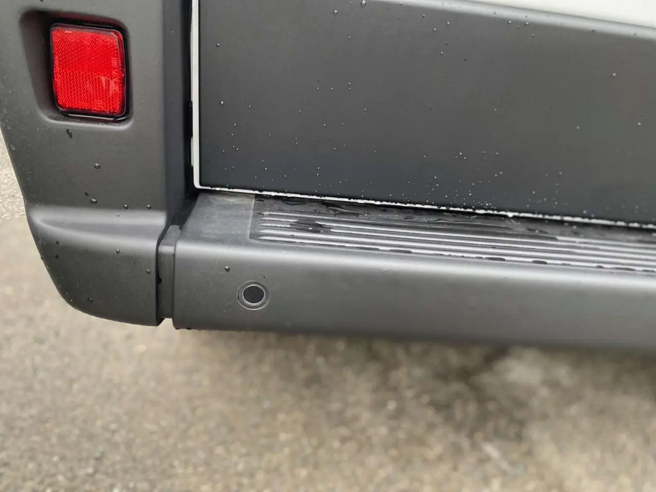 Gros plan sur le pare-chocs arrière gris foncé du Citroën Jumper blanc, avec feu arrière et capteur de recul visible.