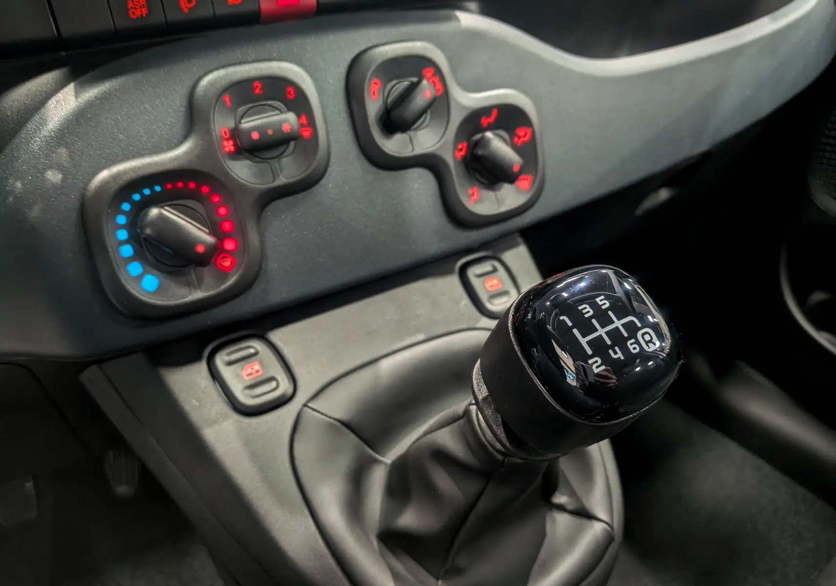 Gros plan sur la commande de la boîte manuelle et les réglages de climatisation du tableau de bord noir de la Fiat Panda 2025.