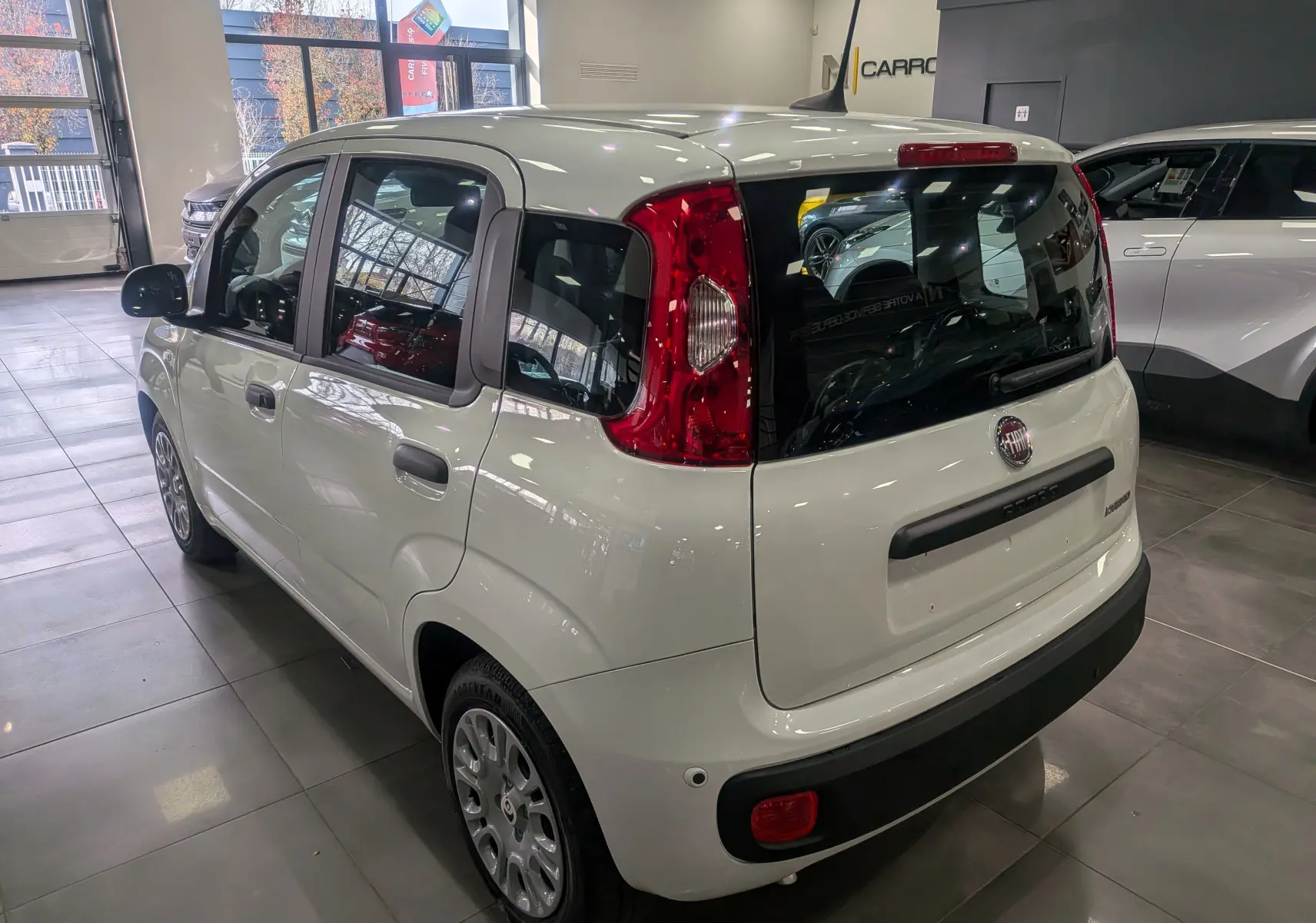 Vue 3/4 arrière droite d'une FIAT Panda 1.0 Hybrid 2025 en blanc Gelato, avec feux arrière rouges et vitres teintées.