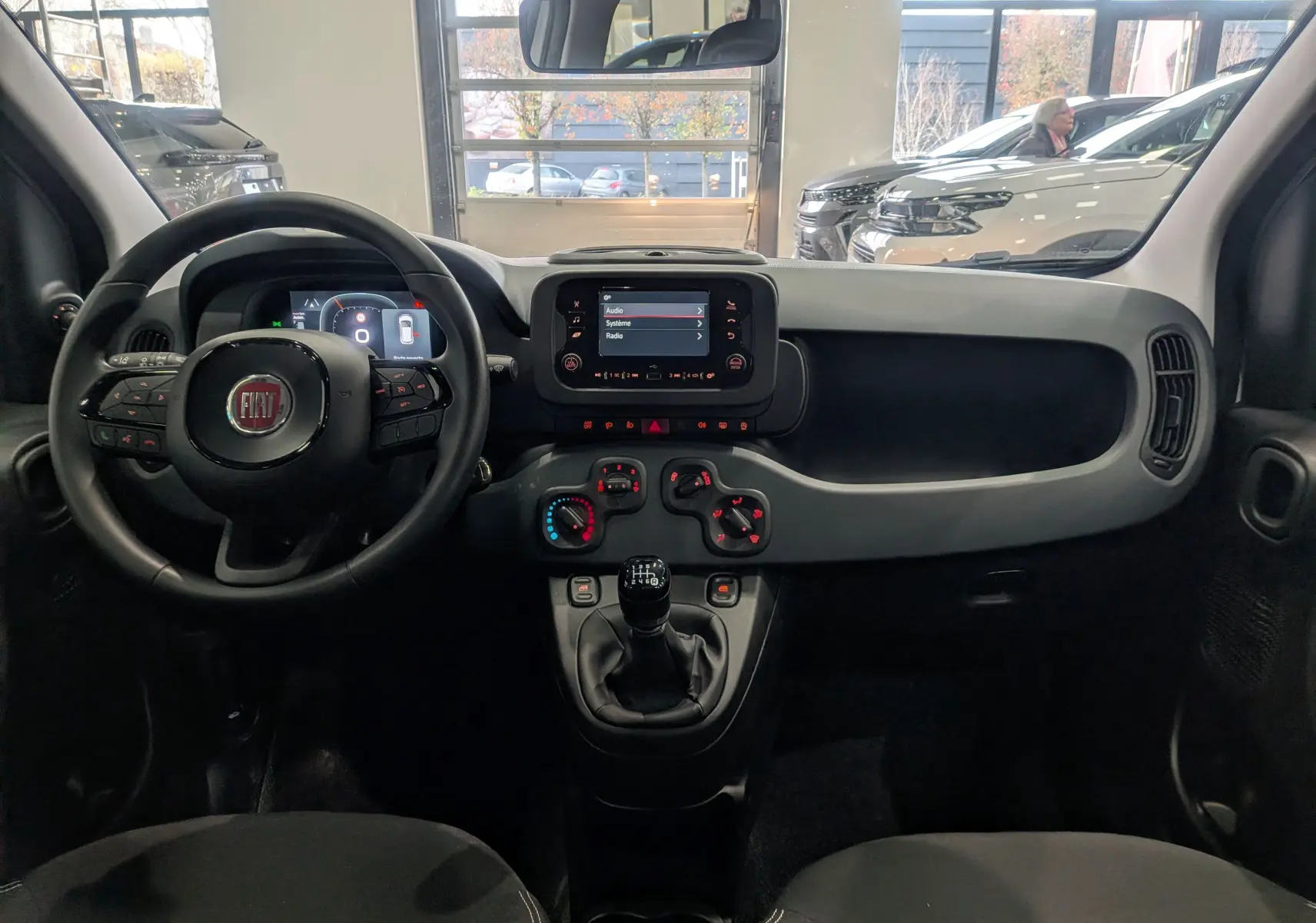 Vue intérieure avant de la Fiat Panda 1.0 Hybrid 2025, tableau de bord noir avec écran tactile et levier de vitesse manuel.