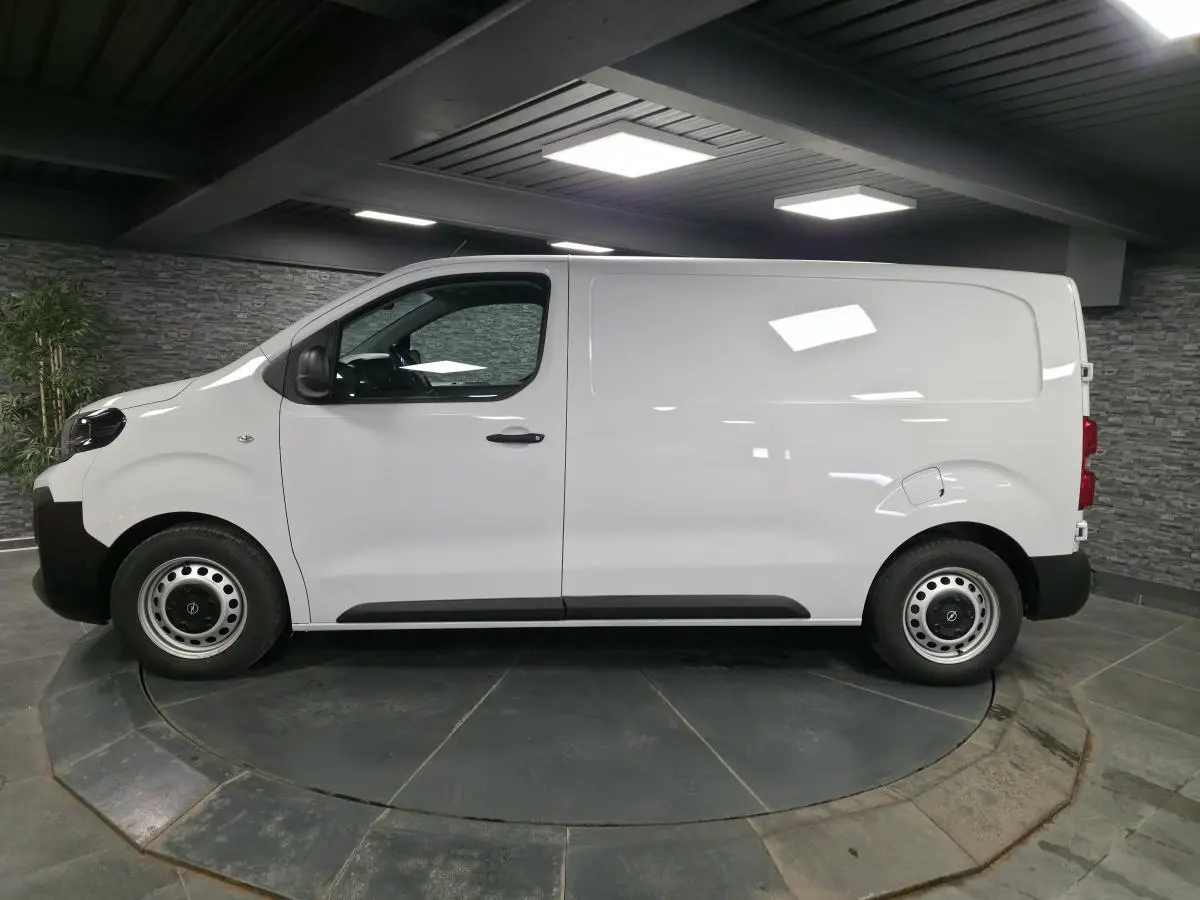 Opel Vivaro blanc en profil droit dans un showroom, avec roues tôles grises et poignées noires.