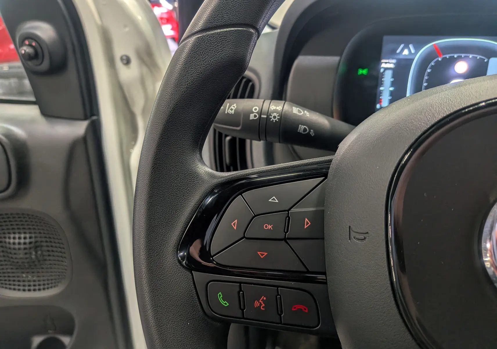 Gros plan sur la partie gauche du volant noir de la Fiat Panda 1.0 Hybrid 2025, avec commandes intégrées et tableau de bord en arrière-plan.