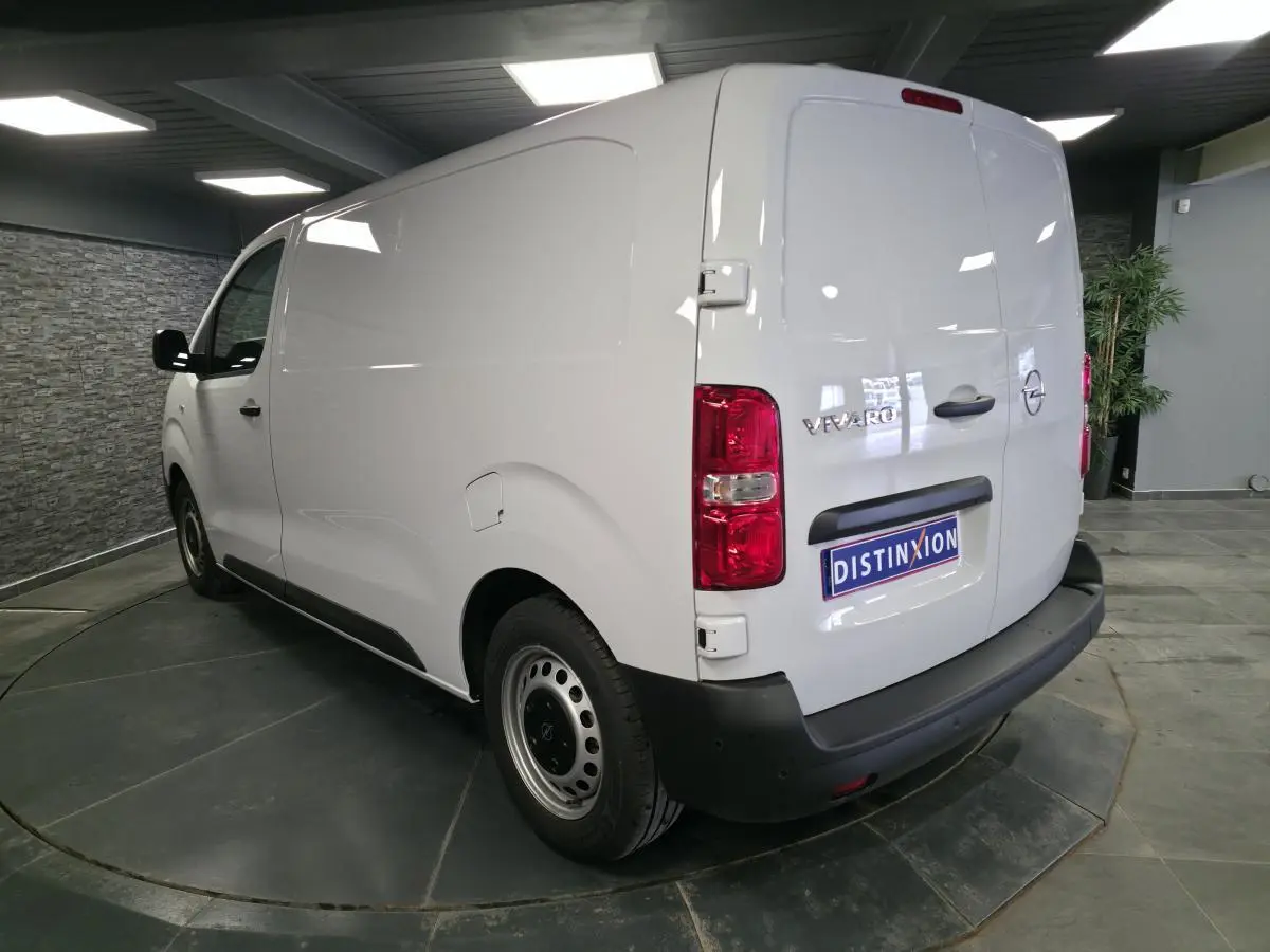 Vue 3/4 arrière droite d’un Opel Vivaro blanc avec portes arrière tôlées et roues tôles grises en intérieur showroom.