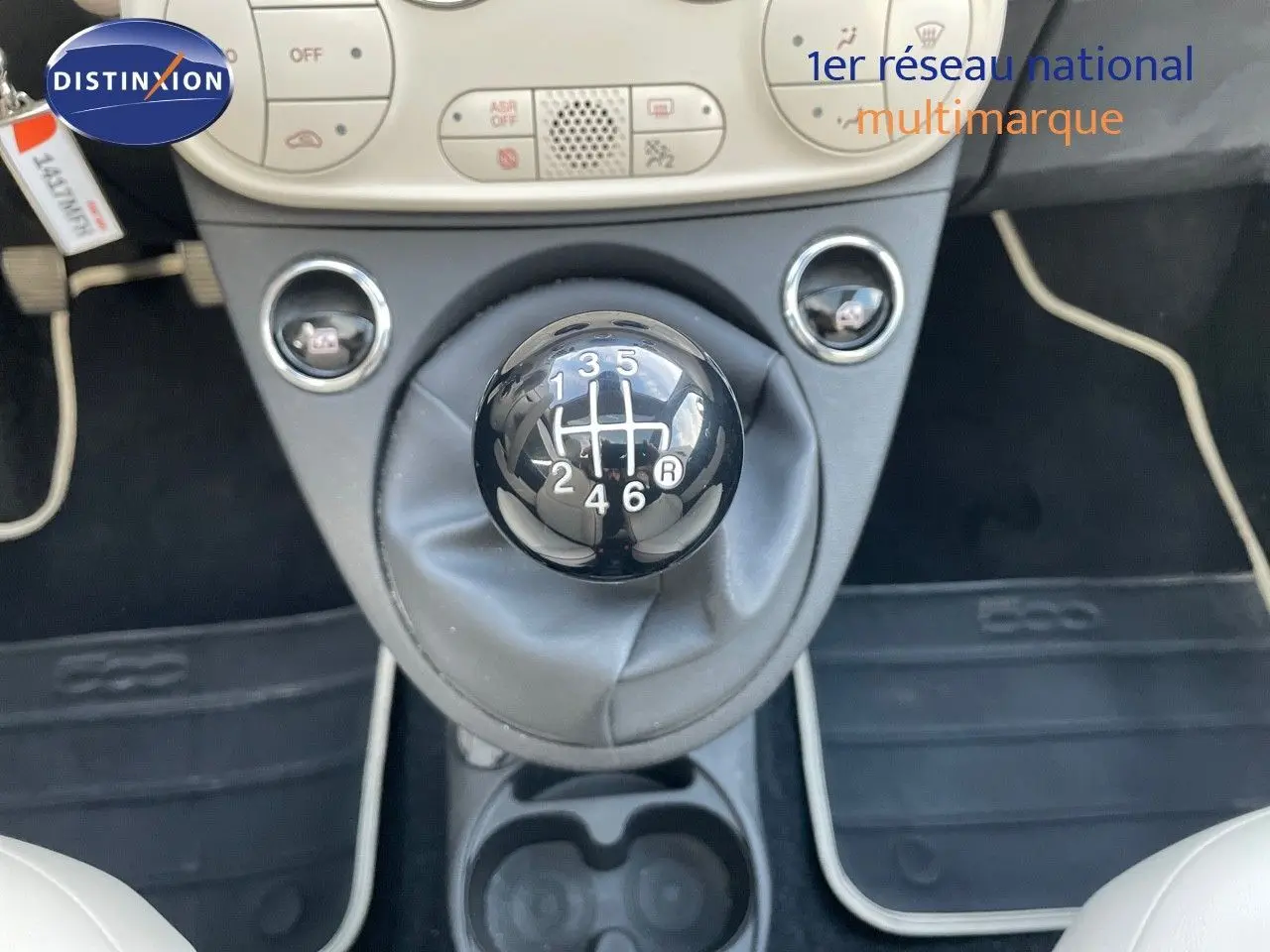 Le levier de vitesses manuel noir au centre de l'habitacle d'une Fiat 500 blanche, avec la console et les commandes climatiques visibles.