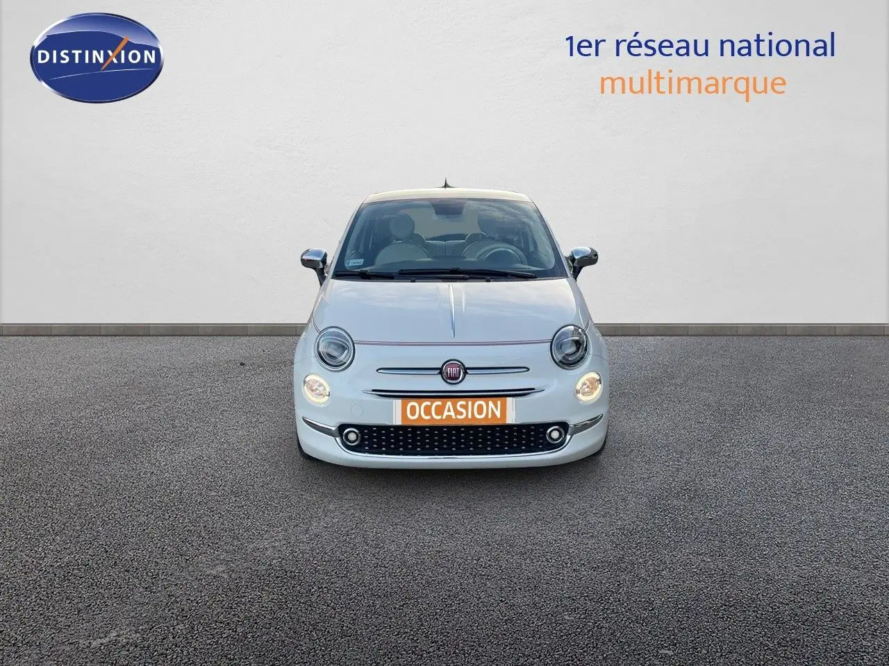 Vue frontale d'une Fiat 500 blanche 1.0 Hybrid 70ch DolceVita avec phares allumés et plaque occasion.