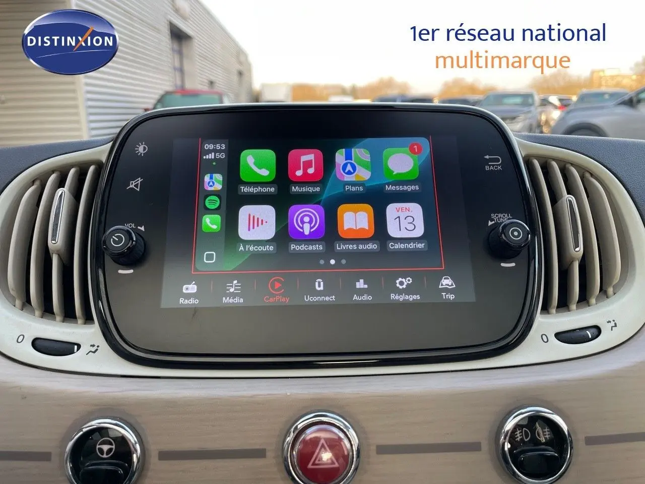 Écran tactile central affichant Apple CarPlay dans l'habitacle clair d'une Fiat 500 blanche, vue de face.