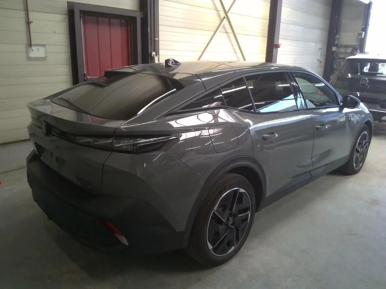 Vue 3/4 arrière droite d'une Peugeot 408 HYBRID 145 GT gris selenium, avec toit noir et jantes distinctives en alliage.
