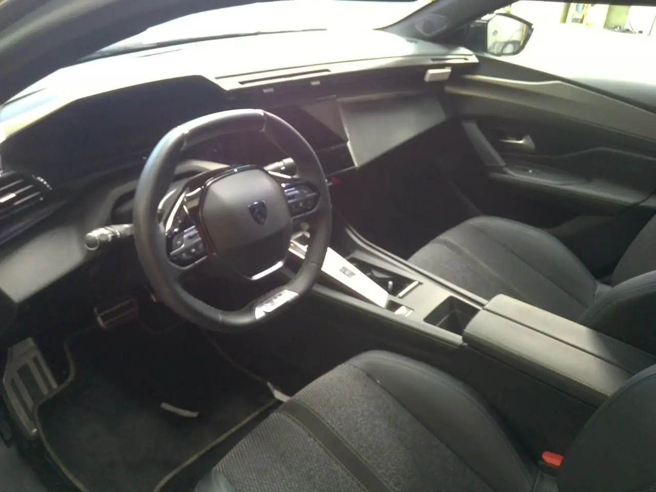 Vue intérieure côté conducteur de la Peugeot 408 Hybrid 145 GT 2025, tableau de bord et volant noirs modernes.