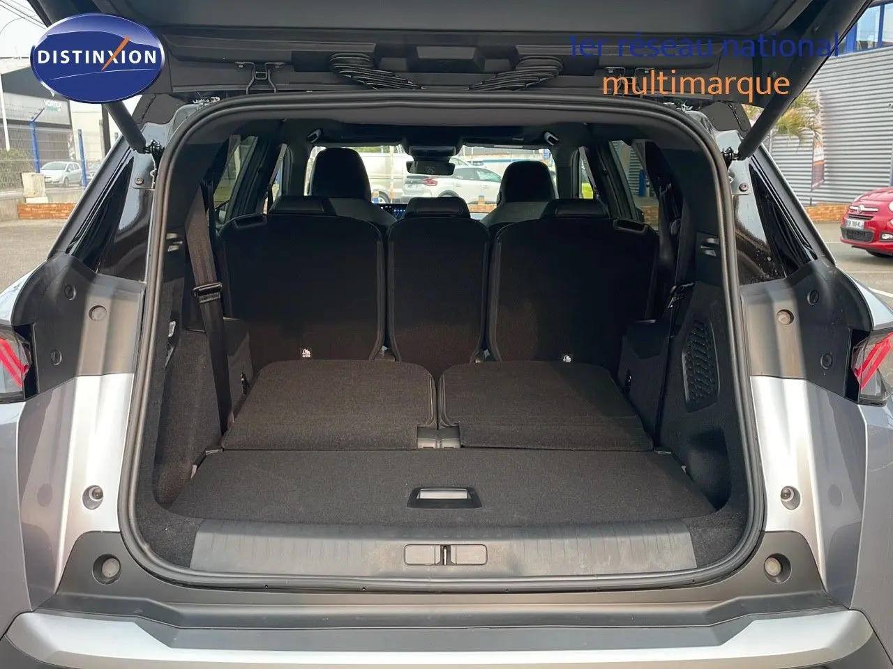 Coffre ouvert d'un Peugeot 5008 gris Artense avec toit noir, montrant les sièges arrière rabattus et l'espace de chargement.