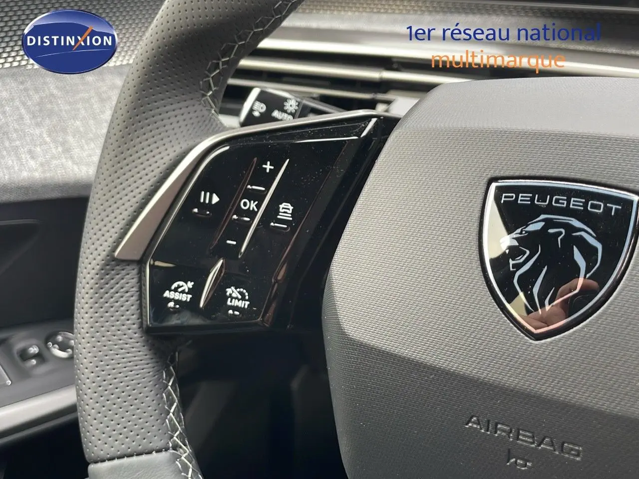 Gros plan sur le volant perforé du Peugeot 5008 Hybrid 2025 avec logo lion et commandes intégrées.