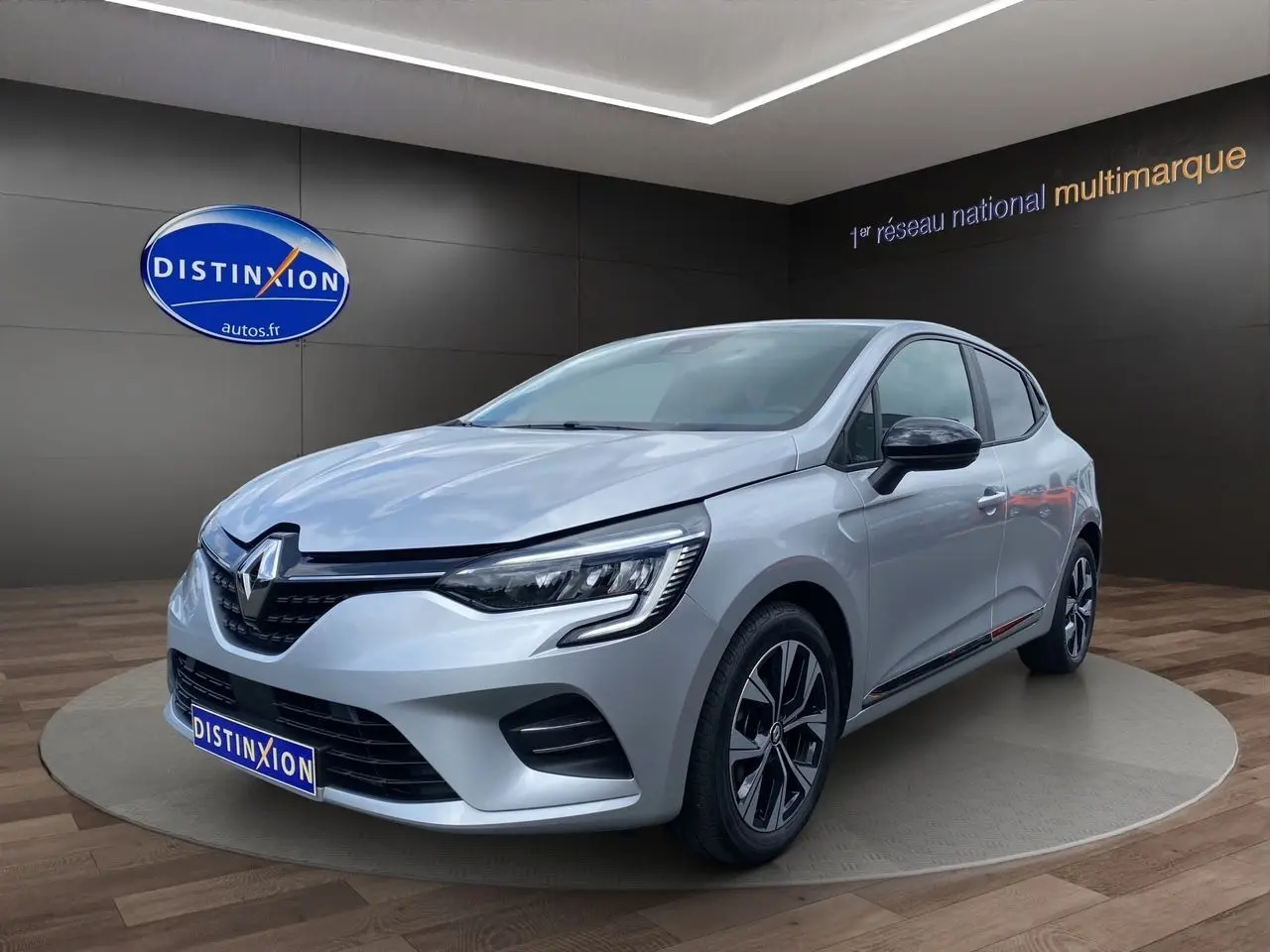 Renault Clio V TCE 90 gris Highland vue 3/4 avant droit, jantes alliage et feux LED distinctifs visibles.