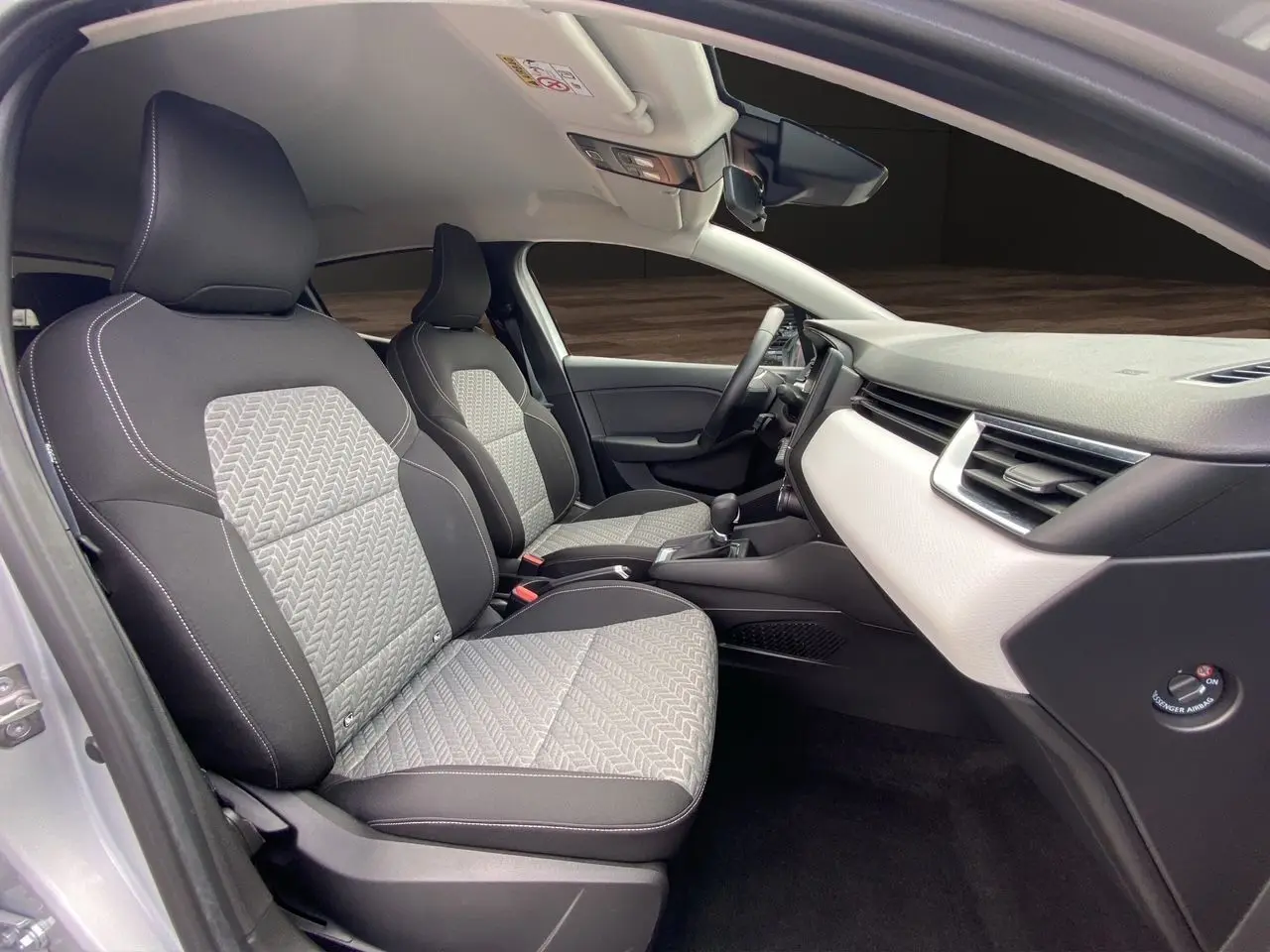 Intérieur avant de la Renault Clio V gris Highland, sièges tissu noir et gris avec motifs, tableau de bord clair moderne.