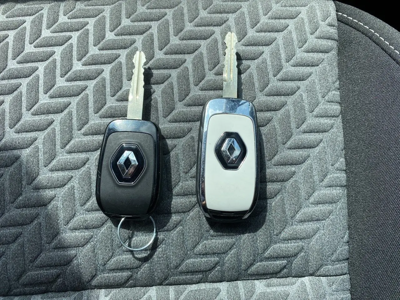 Gros plan sur deux clés Renault posées sur un siège en tissu gris à motif géométrique.