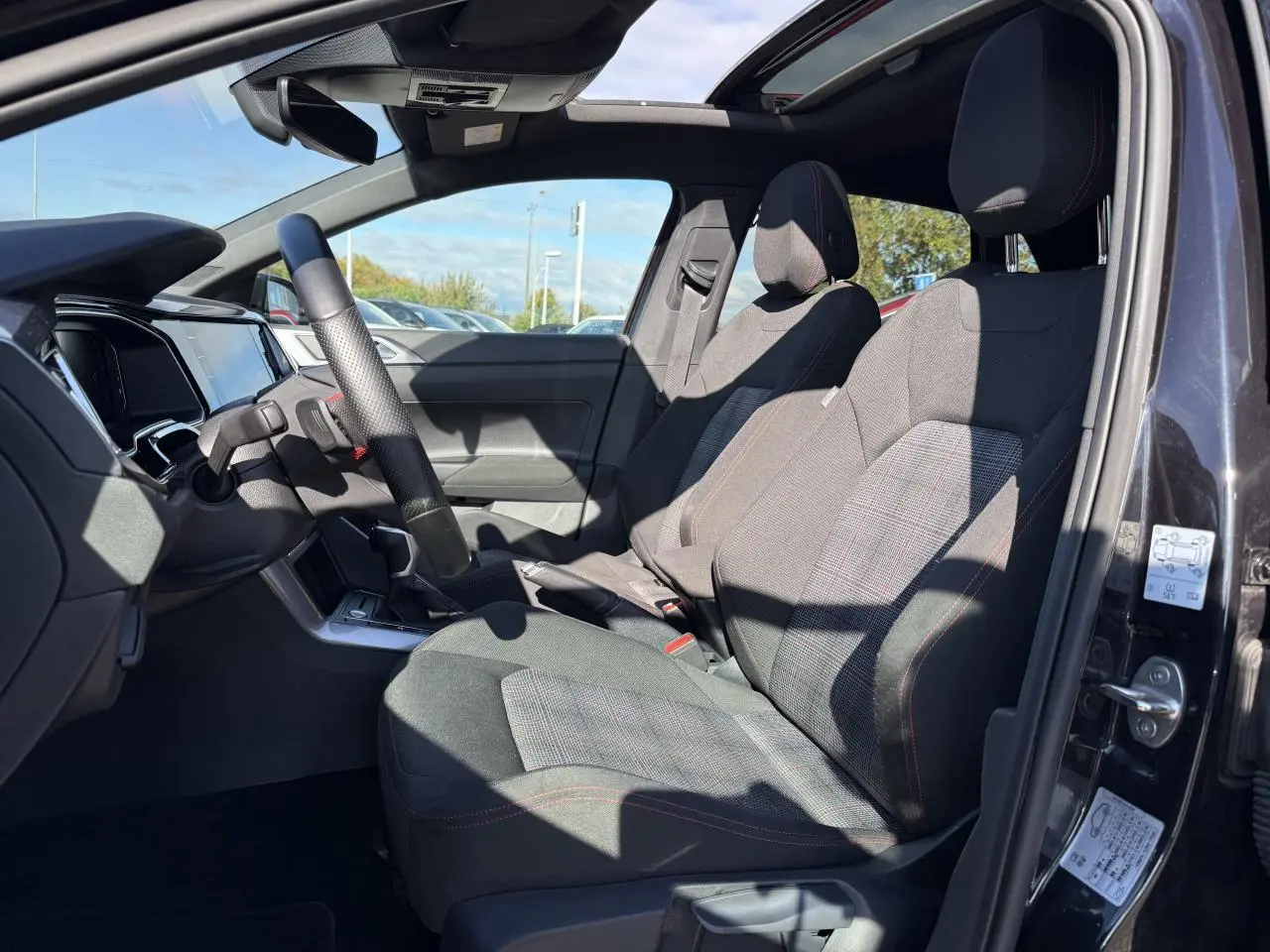 Intérieur côté gauche de la Volkswagen Polo GTI 2024 noir intense nacré, sièges sport et toit ouvrant en verre visible.