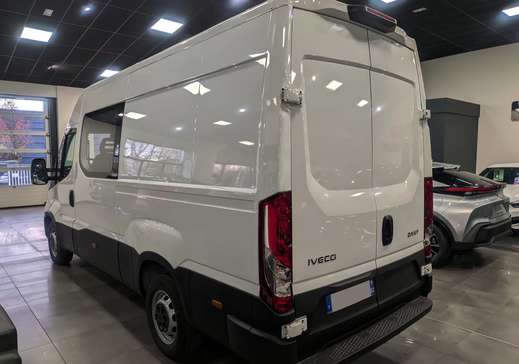 Vue 3/4 arrière droite d'un fourgon Iveco Daily blanc 2025 avec portes arrière fermées dans un showroom.