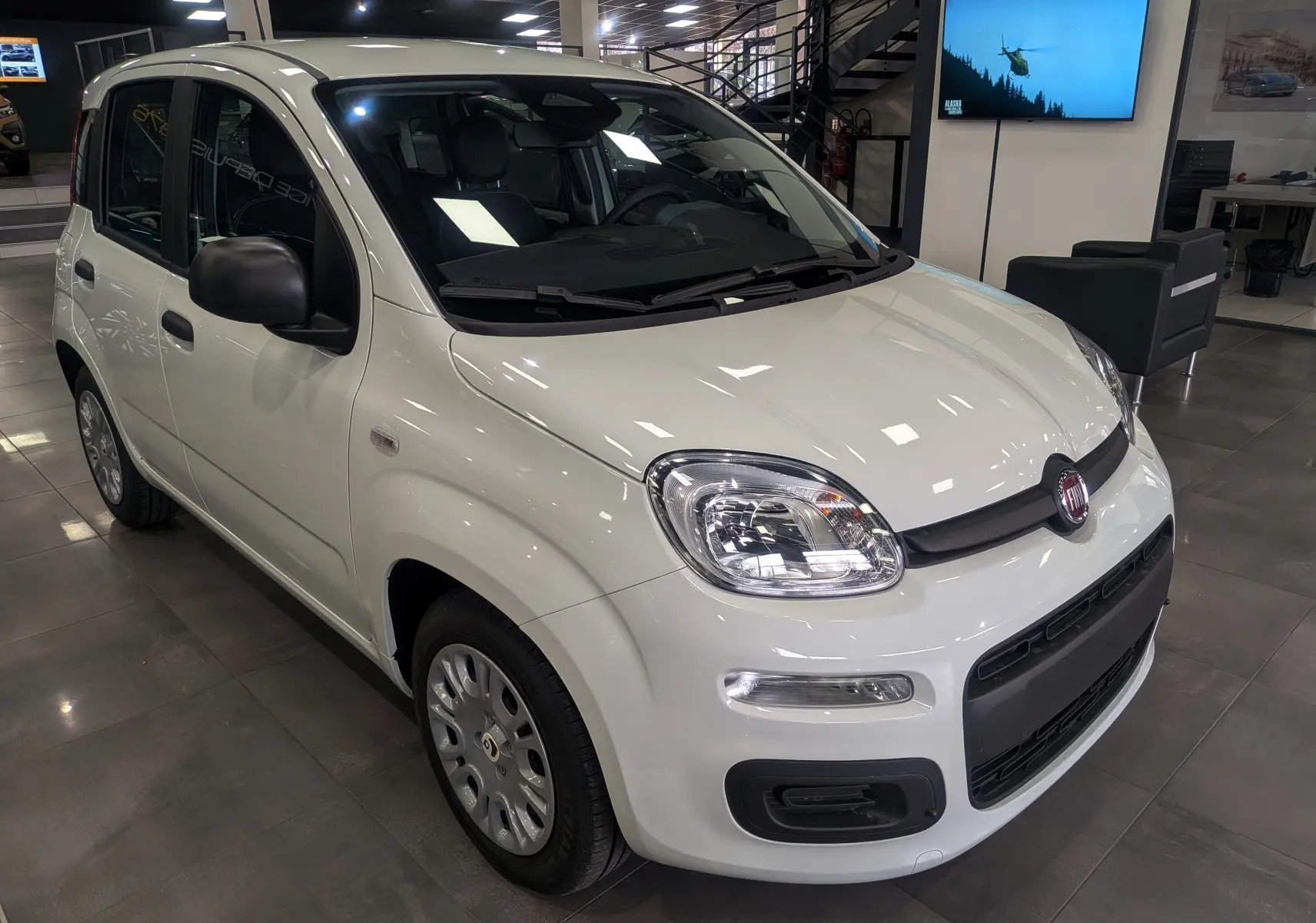 Vue 3/4 avant droite de la FIAT Panda 1.0 70 CH Hybrid City blanche Gelato en showroom, avec rétroviseurs noirs.