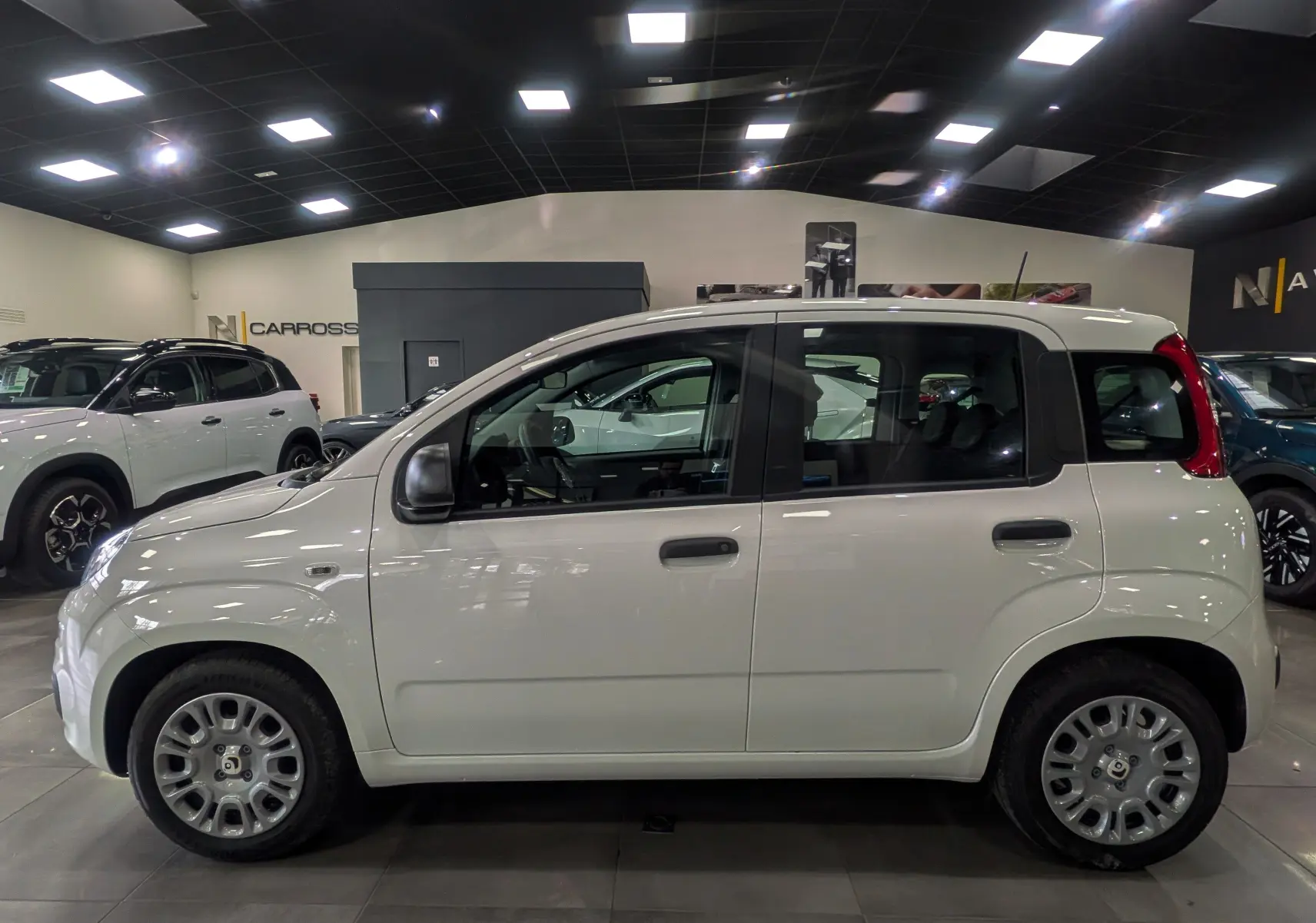 Vue de profil côté gauche d'une Fiat Panda 1.0 70 CH Hybrid City blanche Gelato en intérieur showroom.
