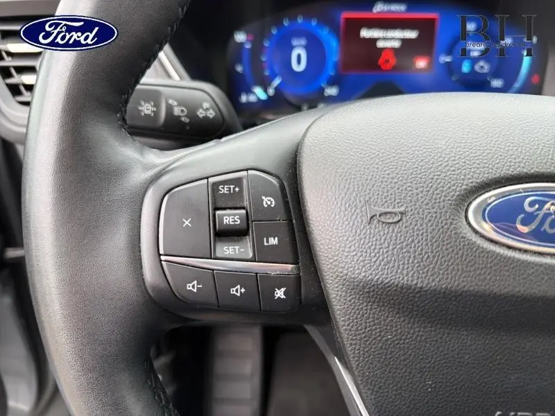 Gros plan sur le volant cuir noir du Ford Kuga 2023 avec commandes multifonctions et tableau de bord numérique bleu.