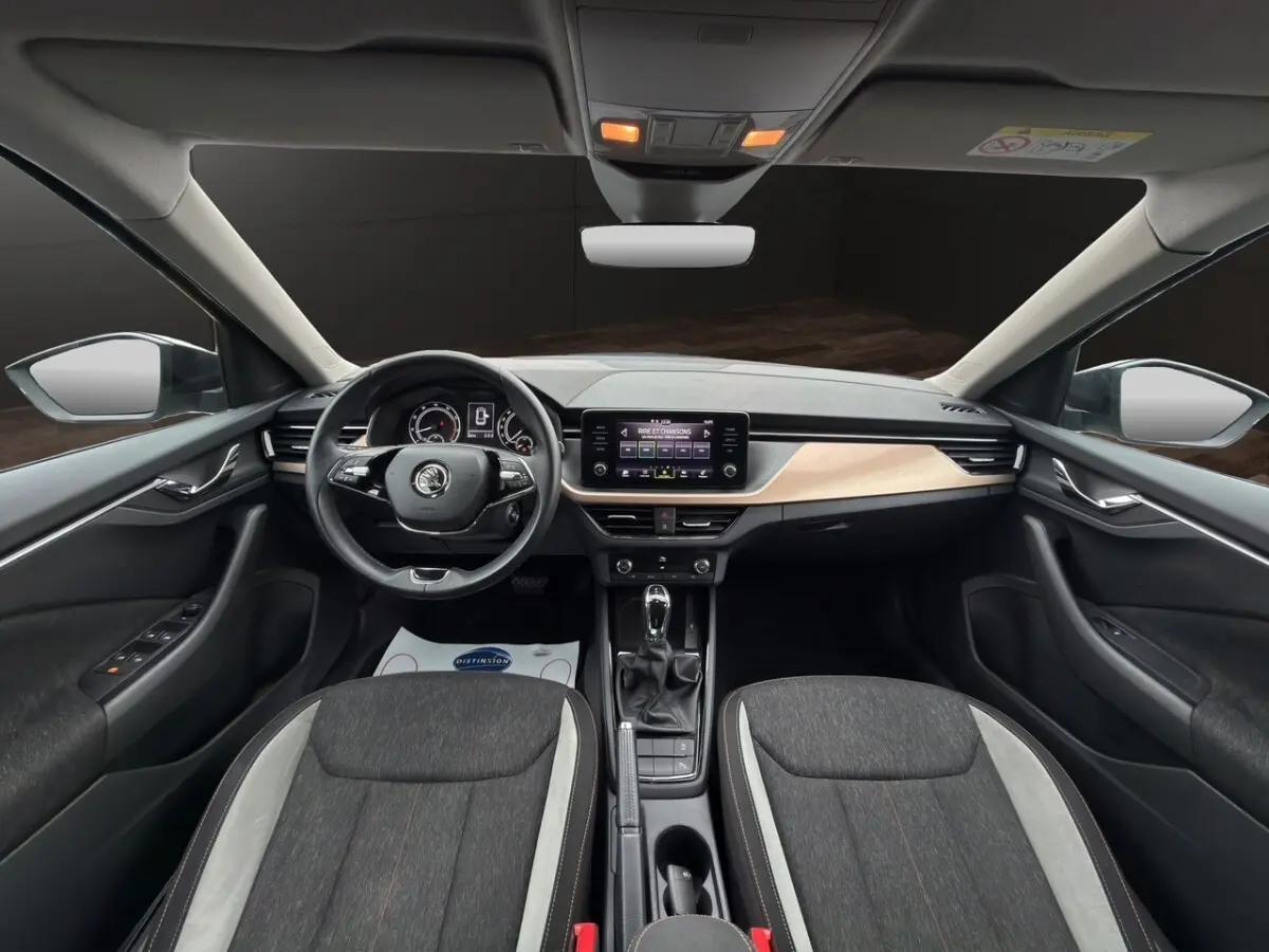 Vue intérieure côté gauche du Skoda Kamiq 2023 gris foncé, sièges tissu bicolore et tableau de bord bois clair.