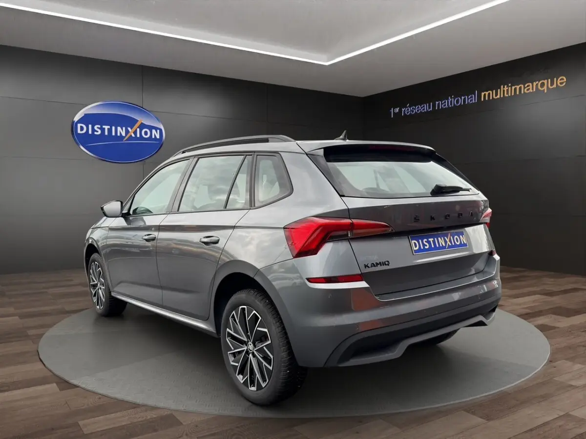 SKODA KAMIQ gris foncé en profil côté gauche, avec jantes bi-ton et toit noir visible en showroom.