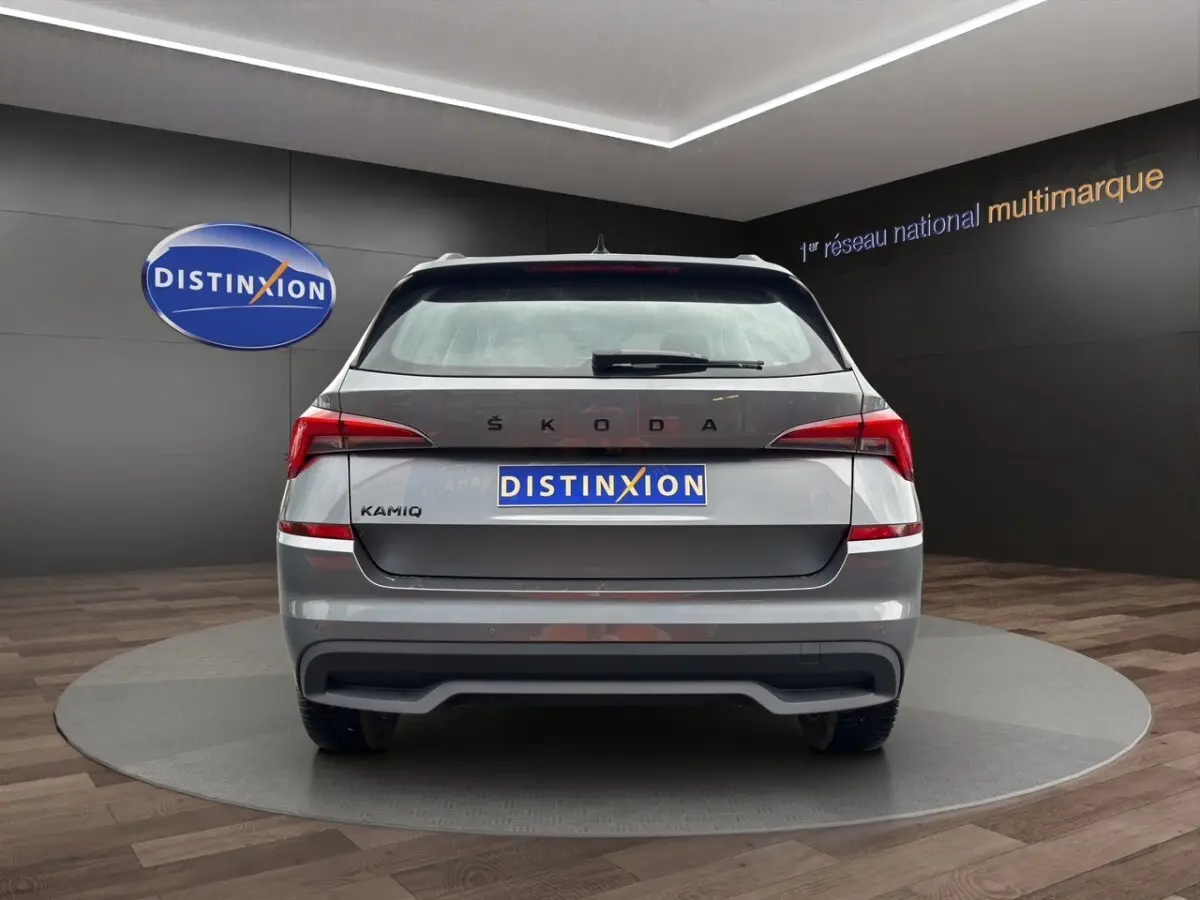 Vue 3/4 arrière droite d'un Skoda Kamiq gris foncé avec jantes bi-ton et caméra de recul en showroom.