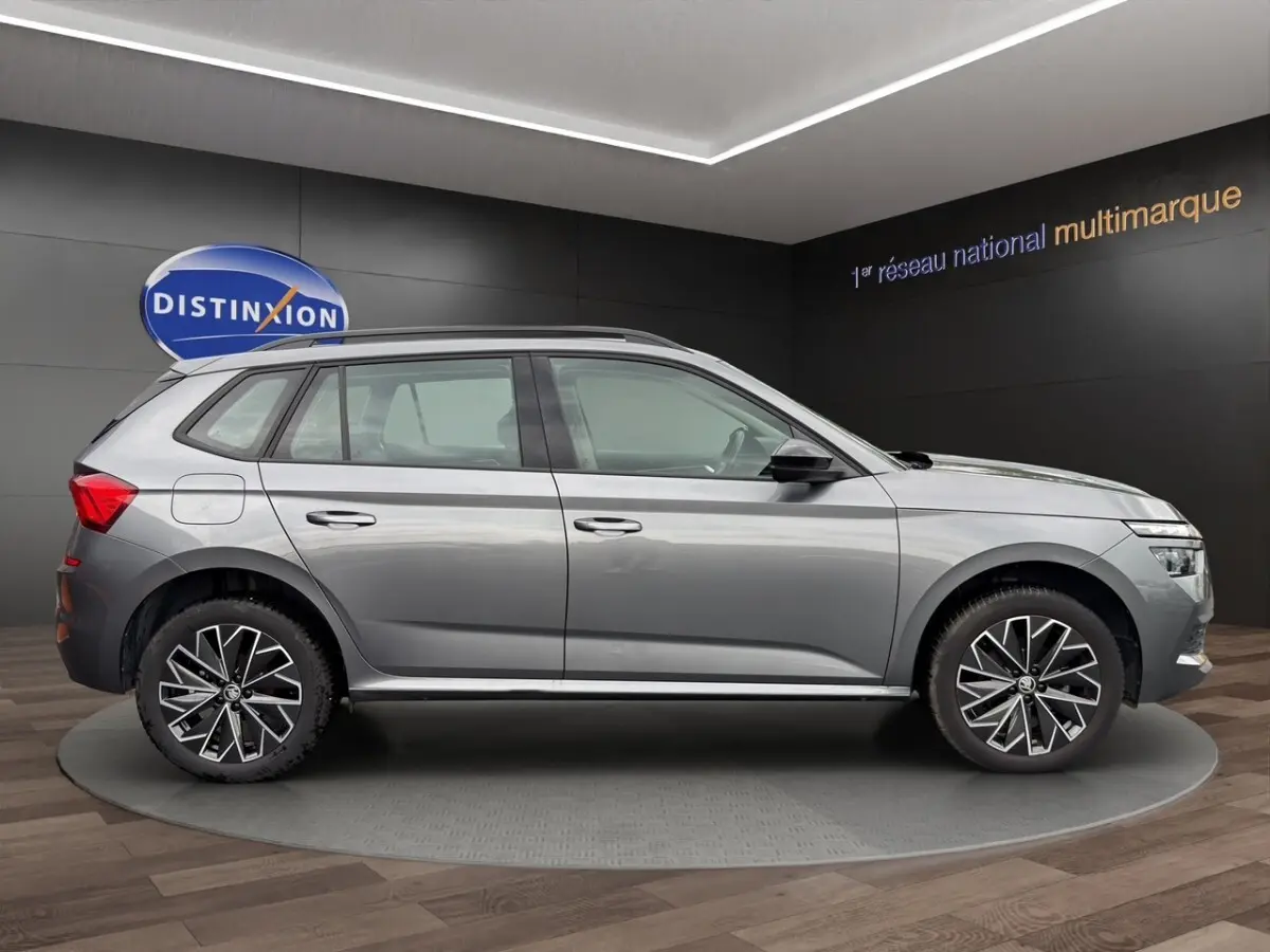 Vue 3/4 arrière droite d'un Skoda Kamiq gris foncé avec jantes bi-ton et caméra de recul en showroom.