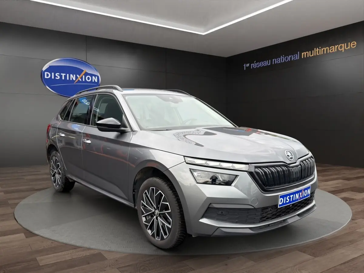 Vue de profil côté gauche d'un Skoda Kamiq gris foncé 2023 avec jantes bi-ton et barres de toit noires.