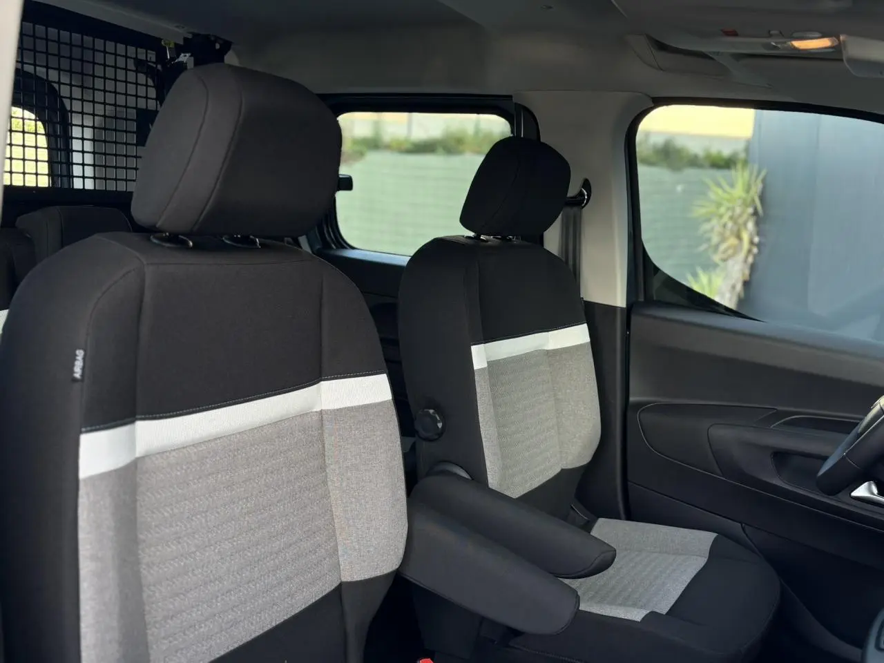 Intérieur avant du Citroën Berlingo Multispace bleu 2025, sièges tissu bicolore avec accoudoirs et séparation métallique.