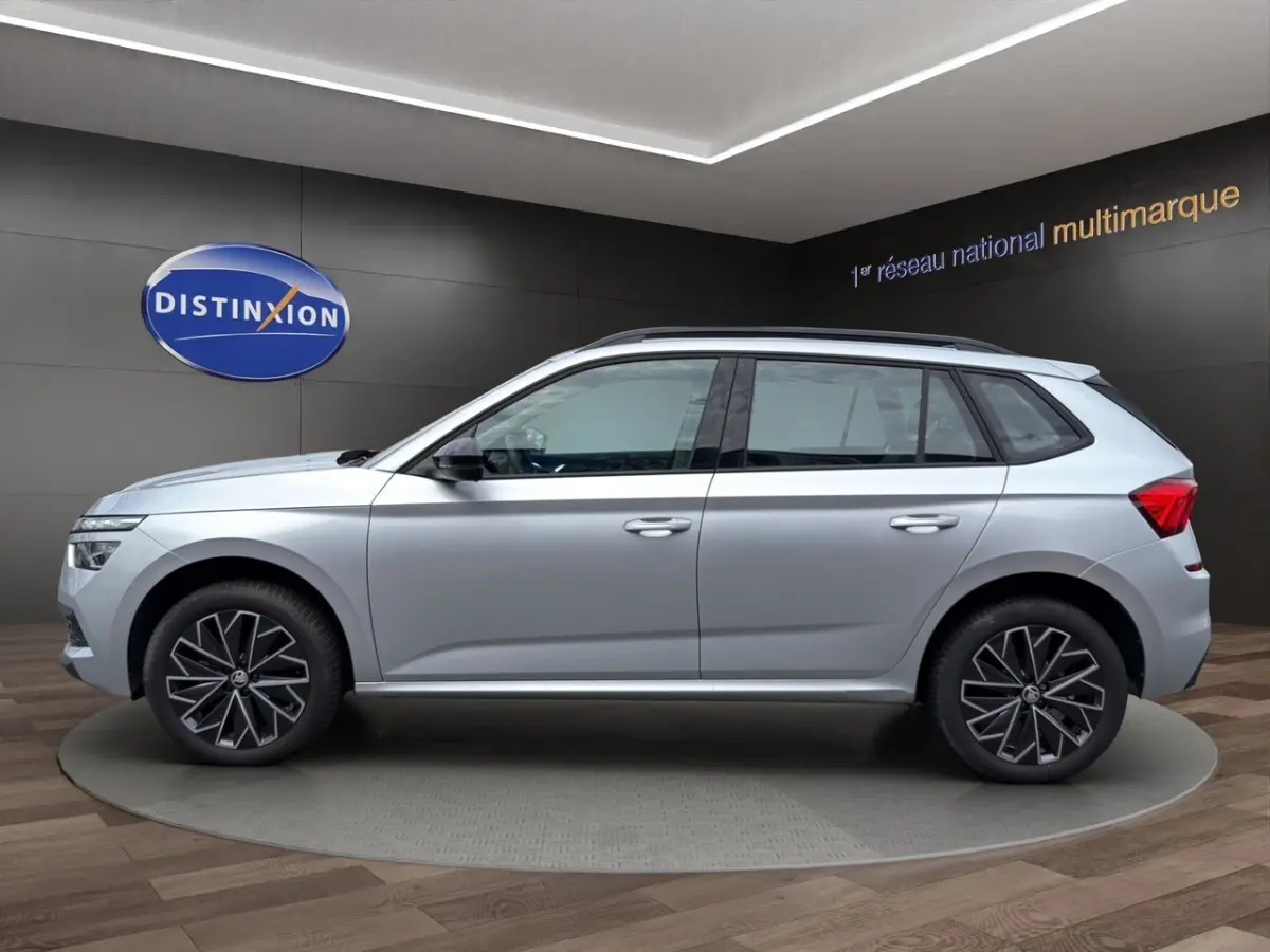 Vue 3/4 avant droite d'un Skoda Kamiq gris clair avec jantes bi-ton et rétroviseurs noirs dans un showroom.