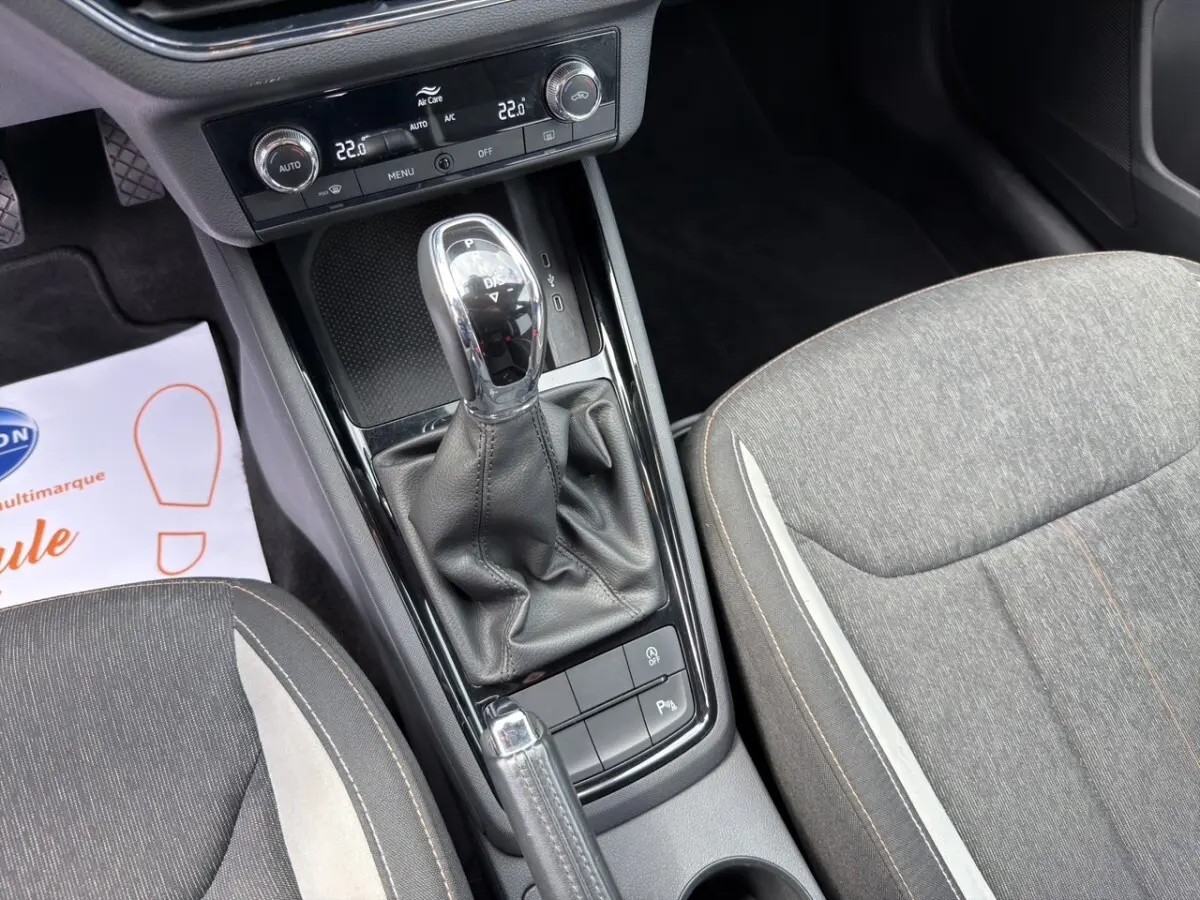 Vue intérieure centrée sur la console centrale avec levier de vitesse automatique et sièges tissu gris du Skoda Kamiq 2023.