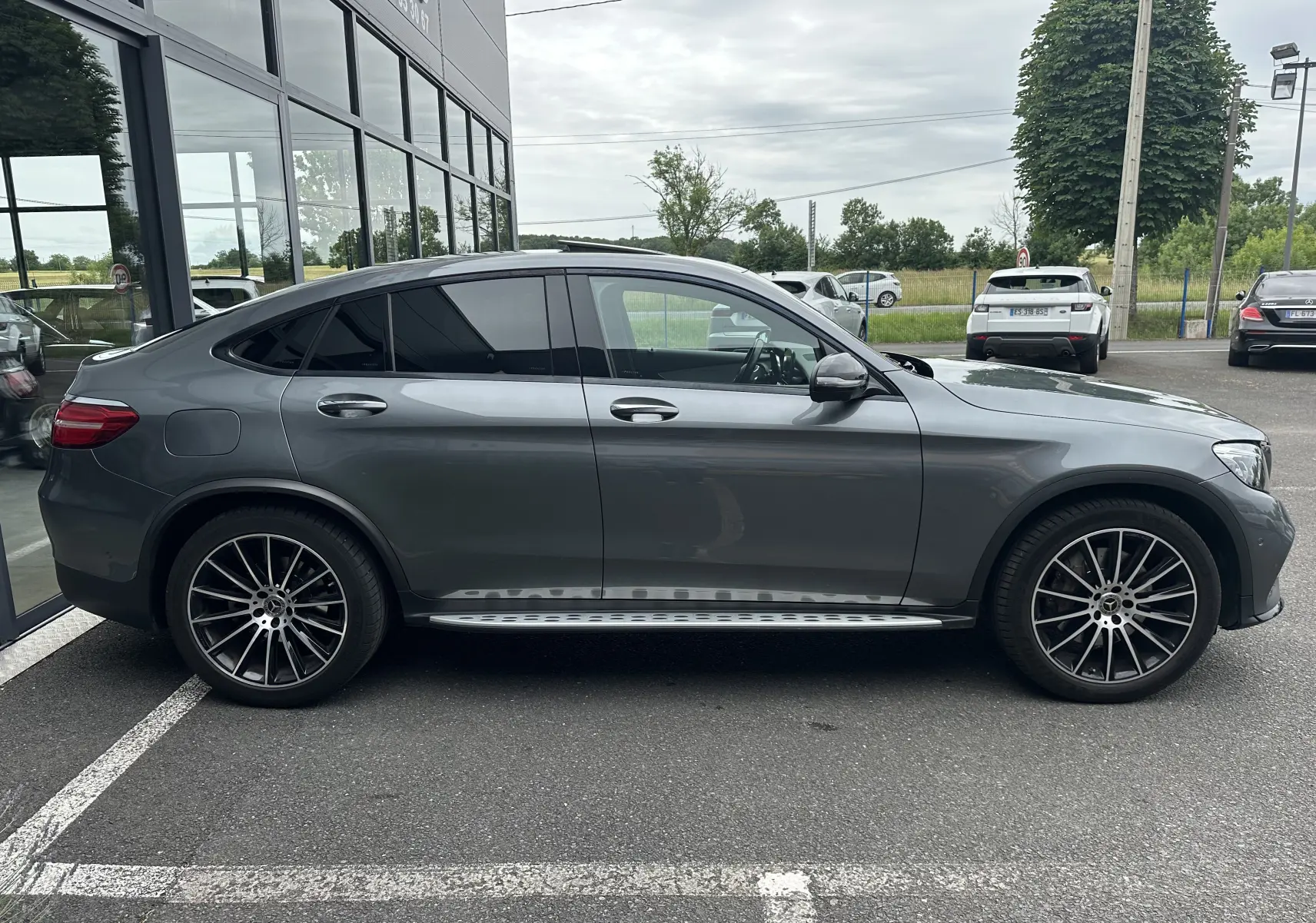 Profil côté gauche d'un Mercedes GLC Coupé 250 D Fascination gris foncé avec jantes alliage et marchepieds visibles.