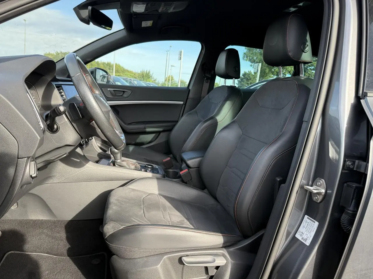 Intérieur côté conducteur du SEAT Ateca gris graphite 2023, sièges sport noirs avec surpiqûres rouges et volant cuir.