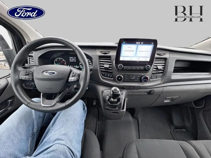 Vue intérieure avant du Ford Transit Custom noir, montrant le volant cuir, tableau de bord et écran tactile central.