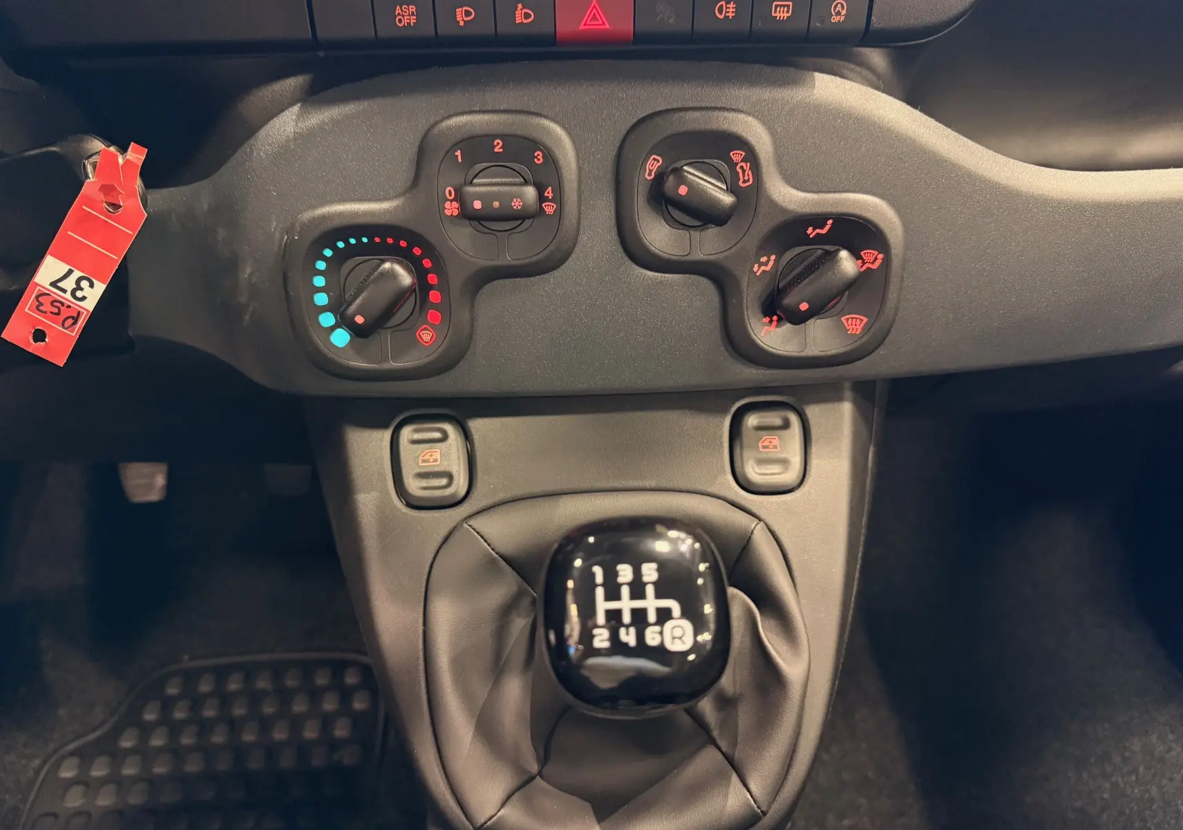 Vue rapprochée du levier de vitesses manuel et des commandes de climatisation d'une Fiat Panda 1.0 Hybrid rouge Amore 2025.