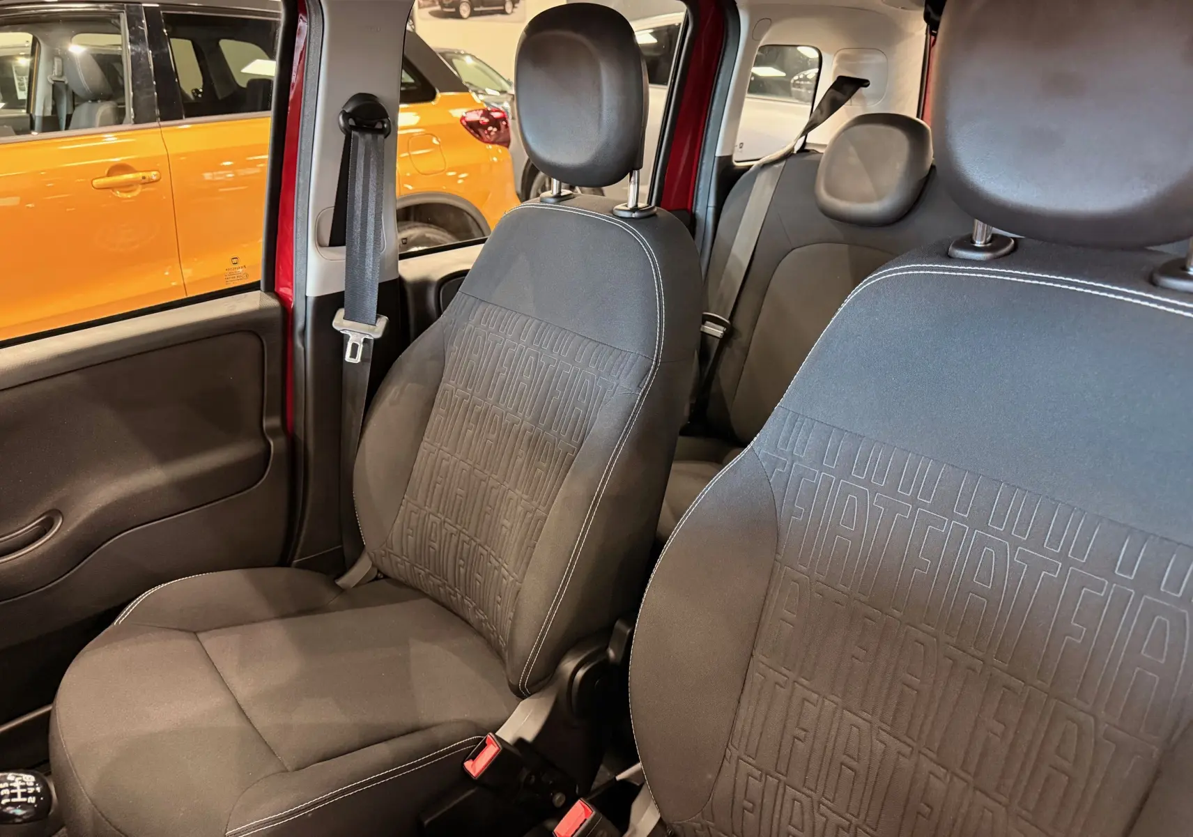 Vue intérieure des sièges avant en tissu noir avec motifs FIAT embossés, portière rouge Amore visible en arrière-plan.