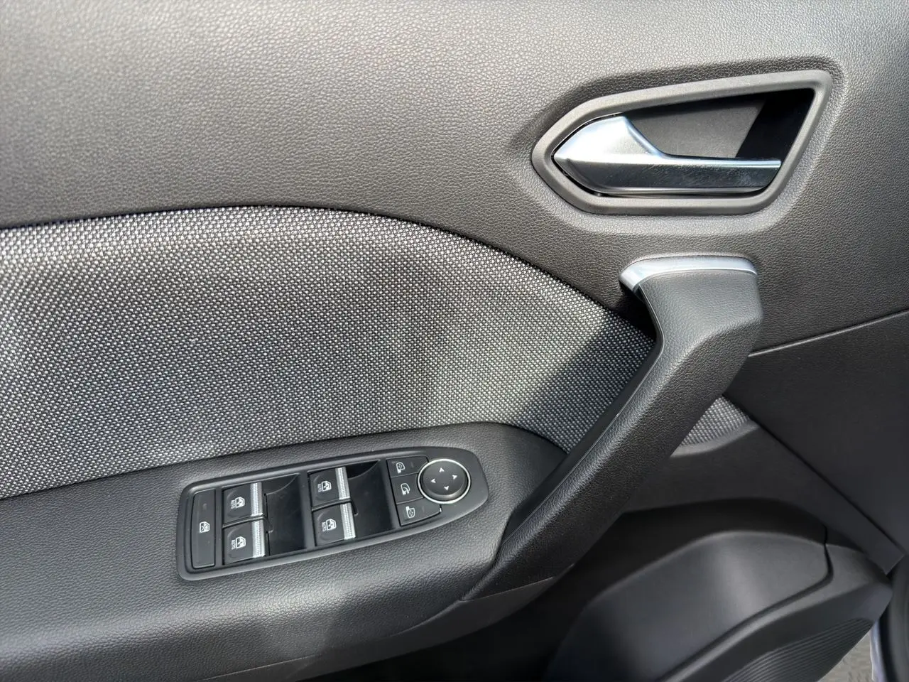 Gros plan sur la porte côté conducteur de la Renault Symbioz gris clair, montrant la poignée et les commandes des vitres électriques.