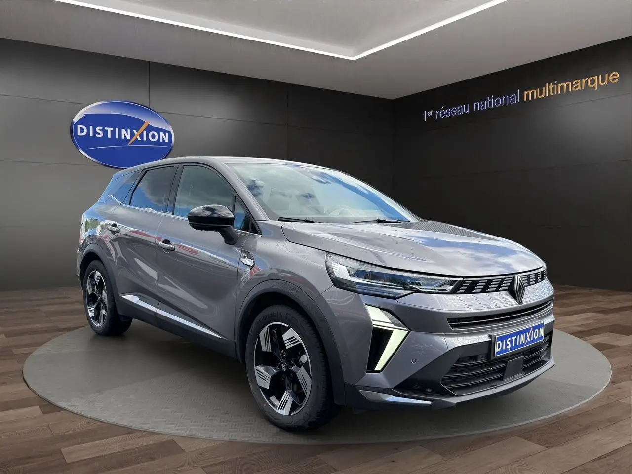 Vue 3/4 avant droit du Renault SYMBIOZ gris clair avec feux LED et jantes noires bicolores sur podium intérieur.