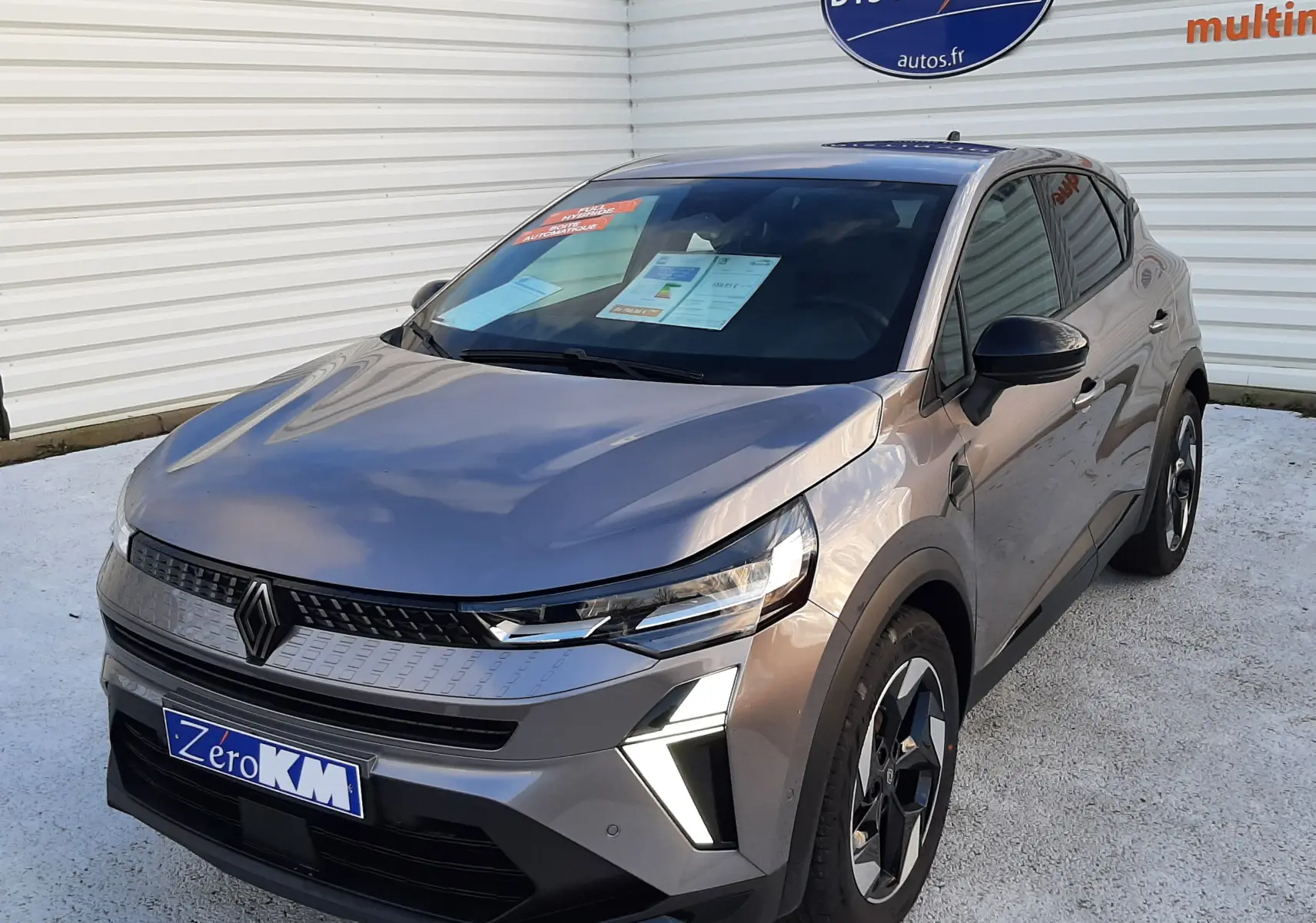 Vue 3/4 avant d’un Renault Captur gris Cassiopée 2025 avec feux LED et jantes bi-ton visibles sur parking.