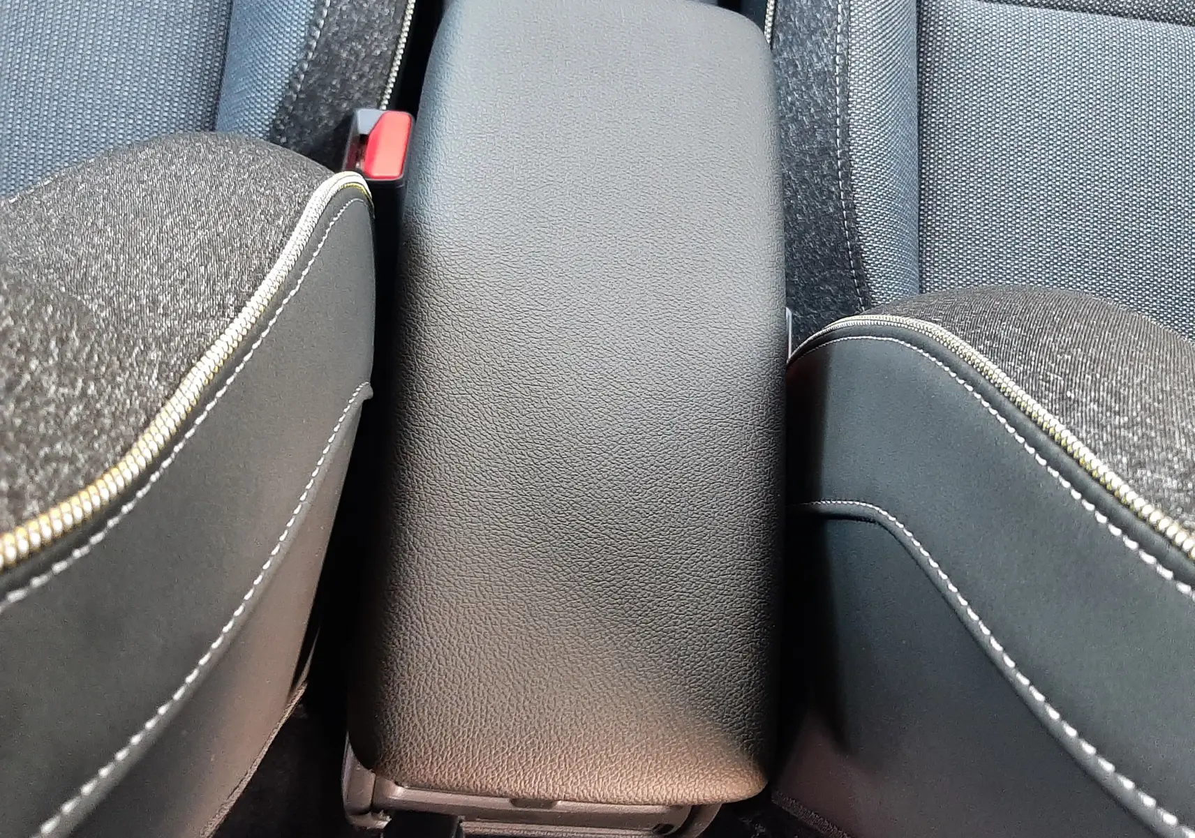 Vue rapprochée de l'accoudoir central en cuir noir entre les sièges avant en tissu gris du Renault Captur 2025.