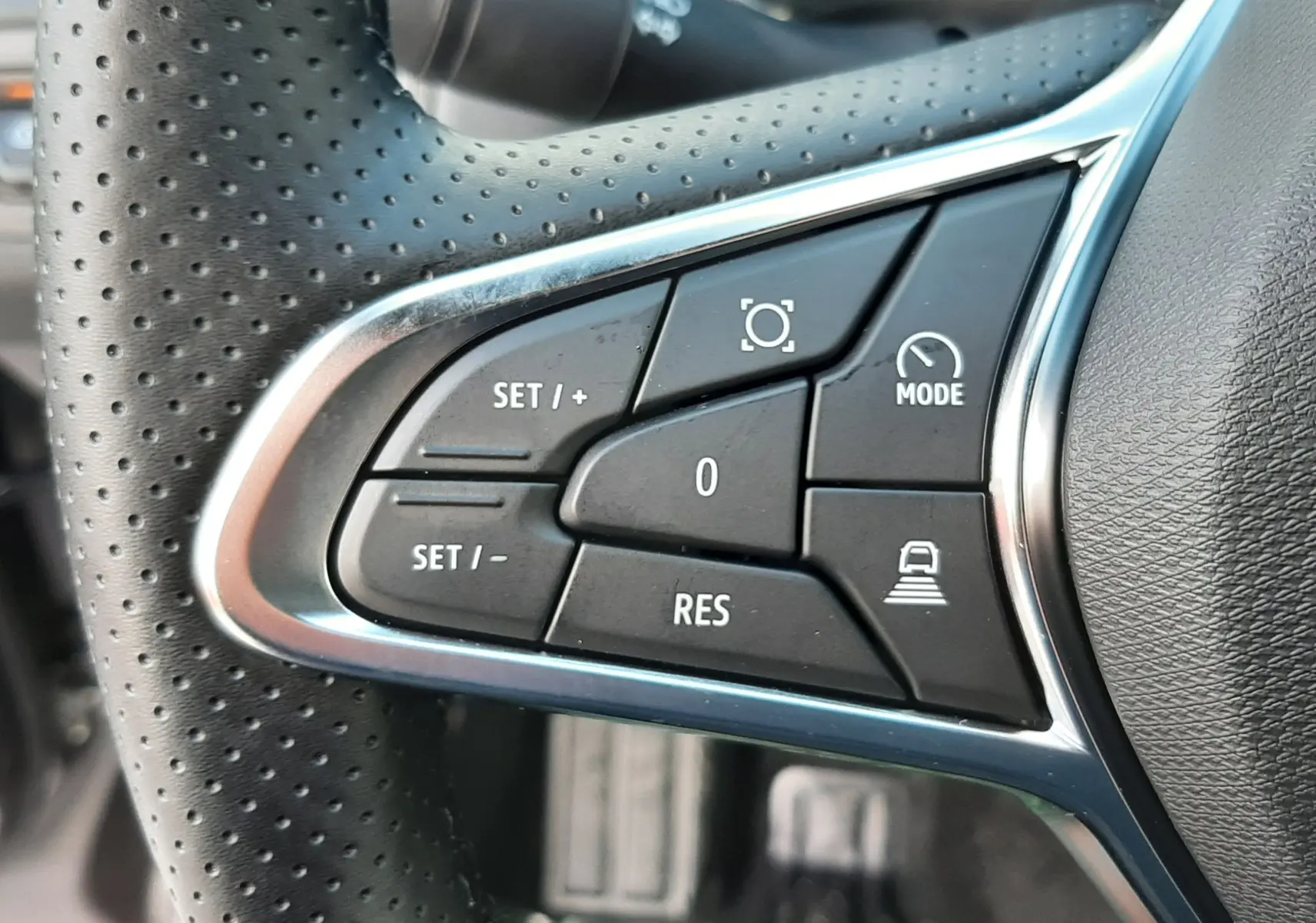 Gros plan sur les commandes multifonctions à gauche du volant perforé du Renault Captur gris Cassiopée 2025.