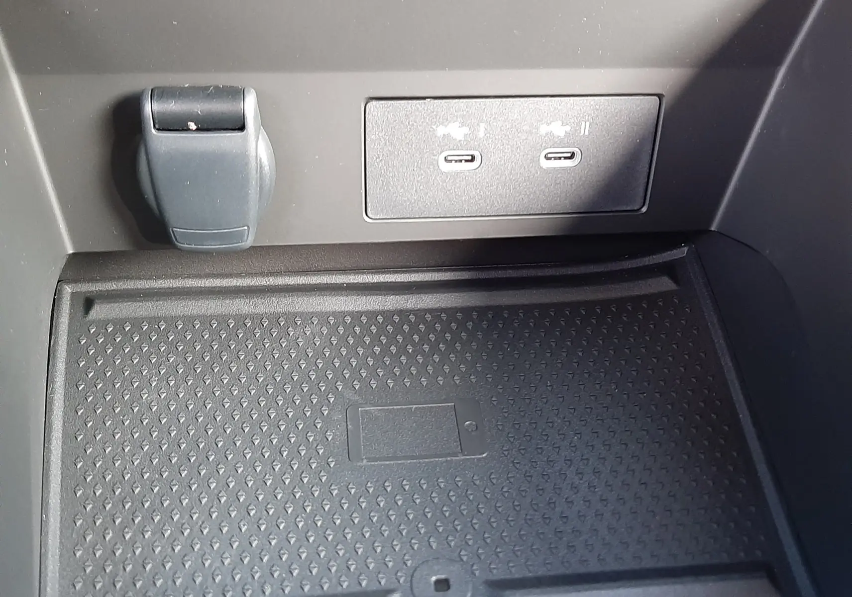 Gros plan sur la console centrale du Renault Captur gris Cassiopée, montrant les ports USB-C et un espace de rangement avec symbole de smartphone.