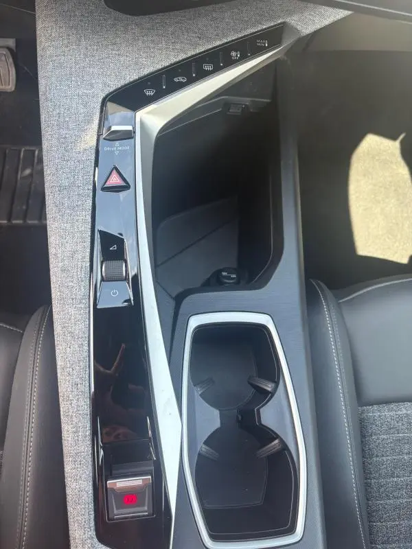 Vue plongeante sur la console centrale grise et noire du Peugeot 3008 Hybrid 136 e-DCS6 Allure 2025 avec commandes tactiles et porte-gobelets.